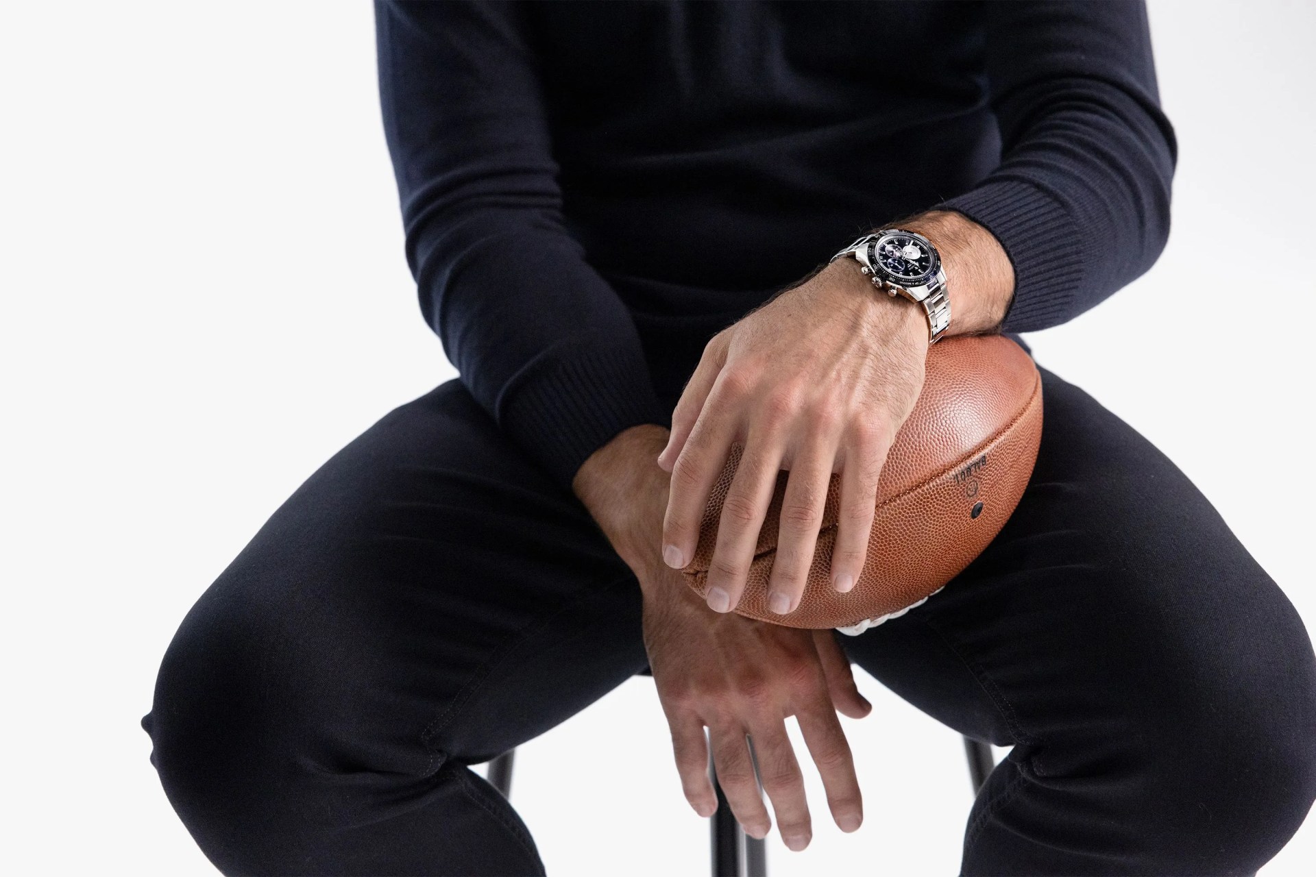 aaron rodgers sitting on a stool wearing a zenith watch and holding a football