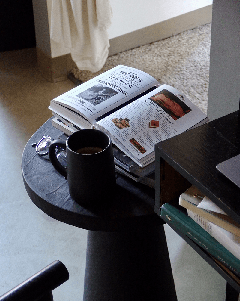 a close up of a side table with magazines a coffee cup and glasses