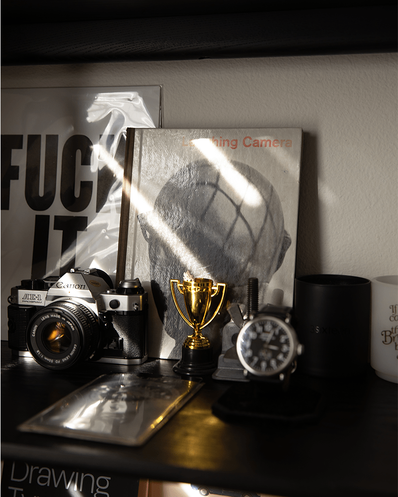 a close up of a black bookshelf with a book, camera, watch and small trophy