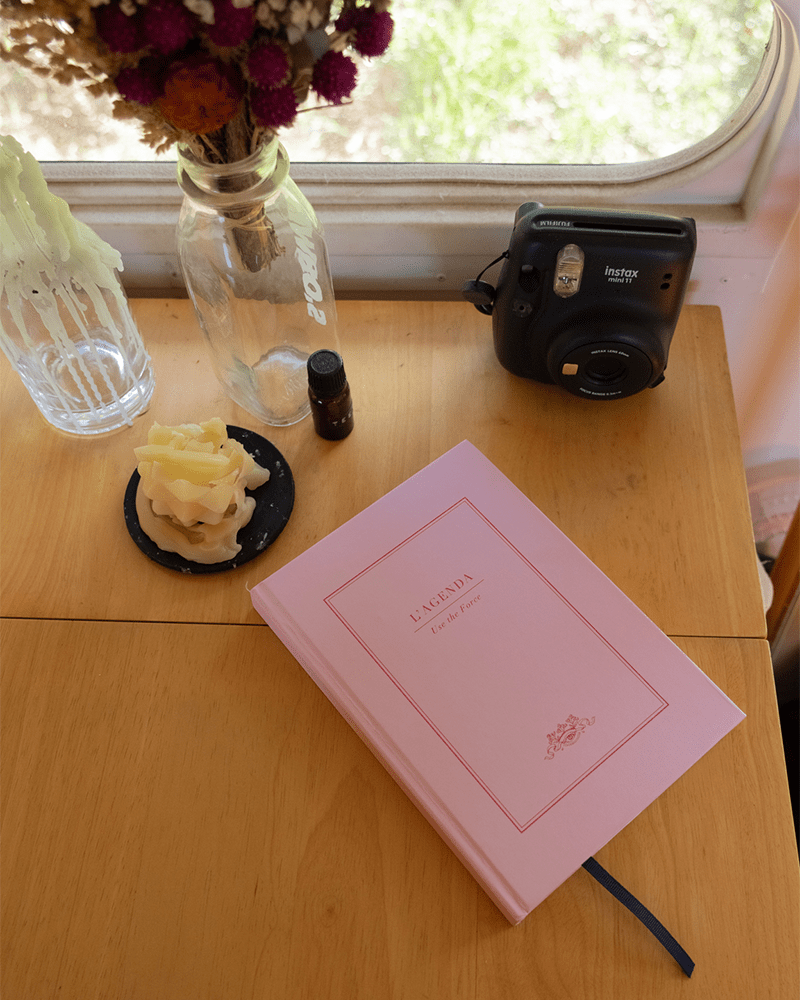 a close up of hayleys wood desk with a pink papier notebook on it