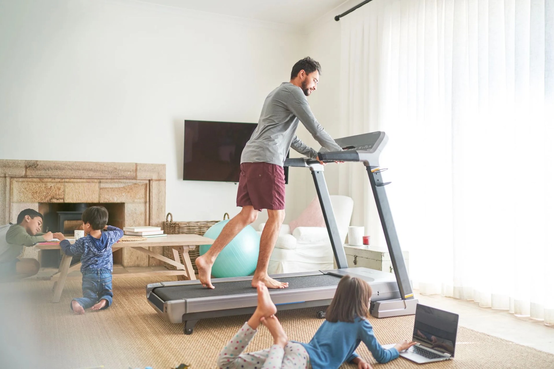 father exercising on treadmill in living room with kids