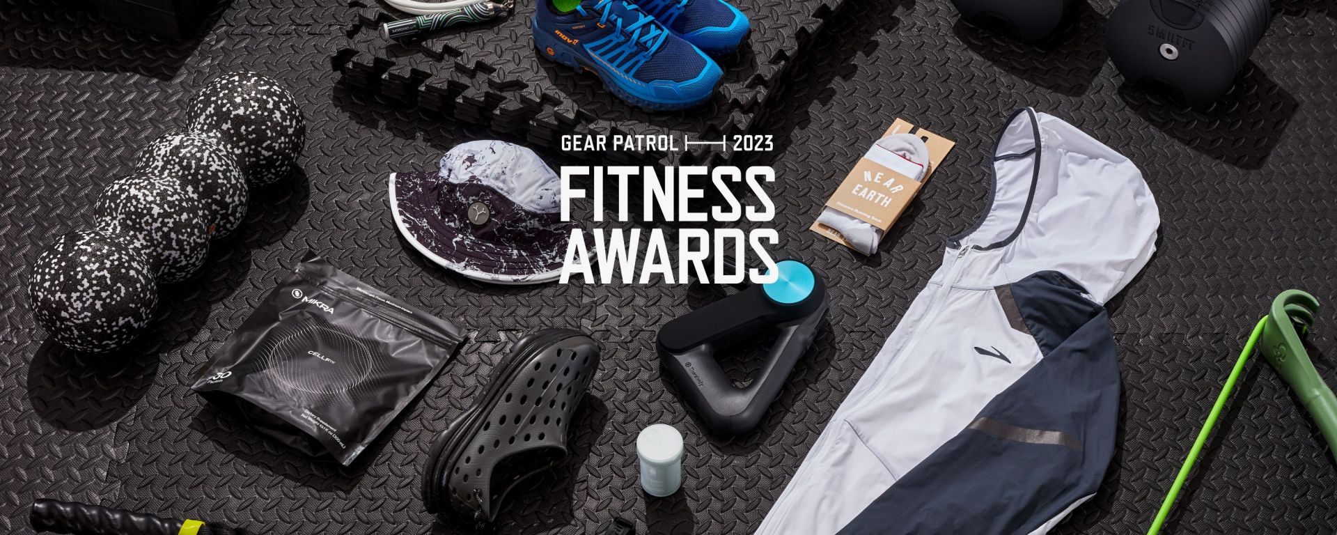 multiple pieces of fitness gear knolled out on top of black rubber gym flooring with text saying 2023 gear patrol fitness awards over top the photo