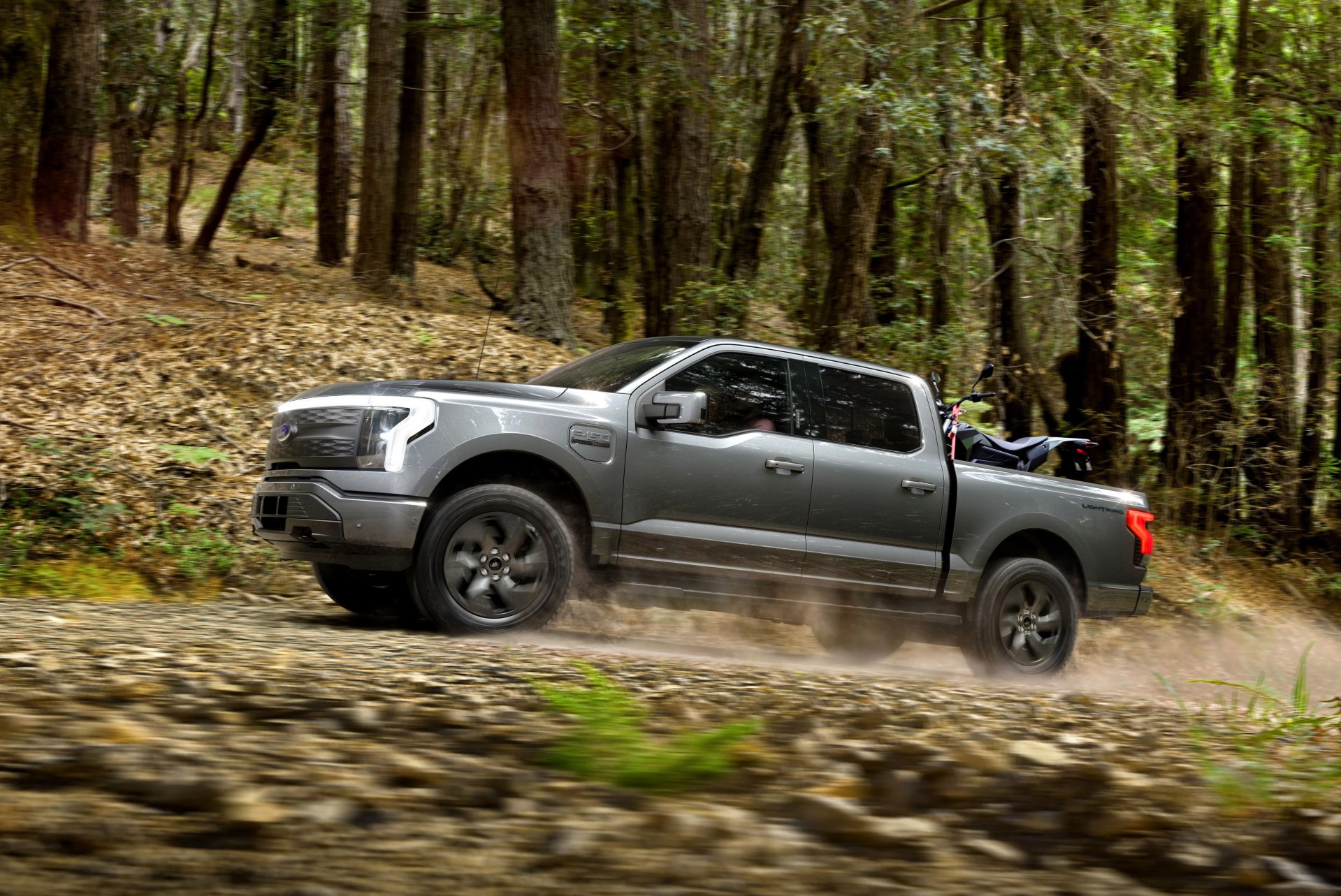 ford f 150 lightning driving in forest with a dirt bike in the bed