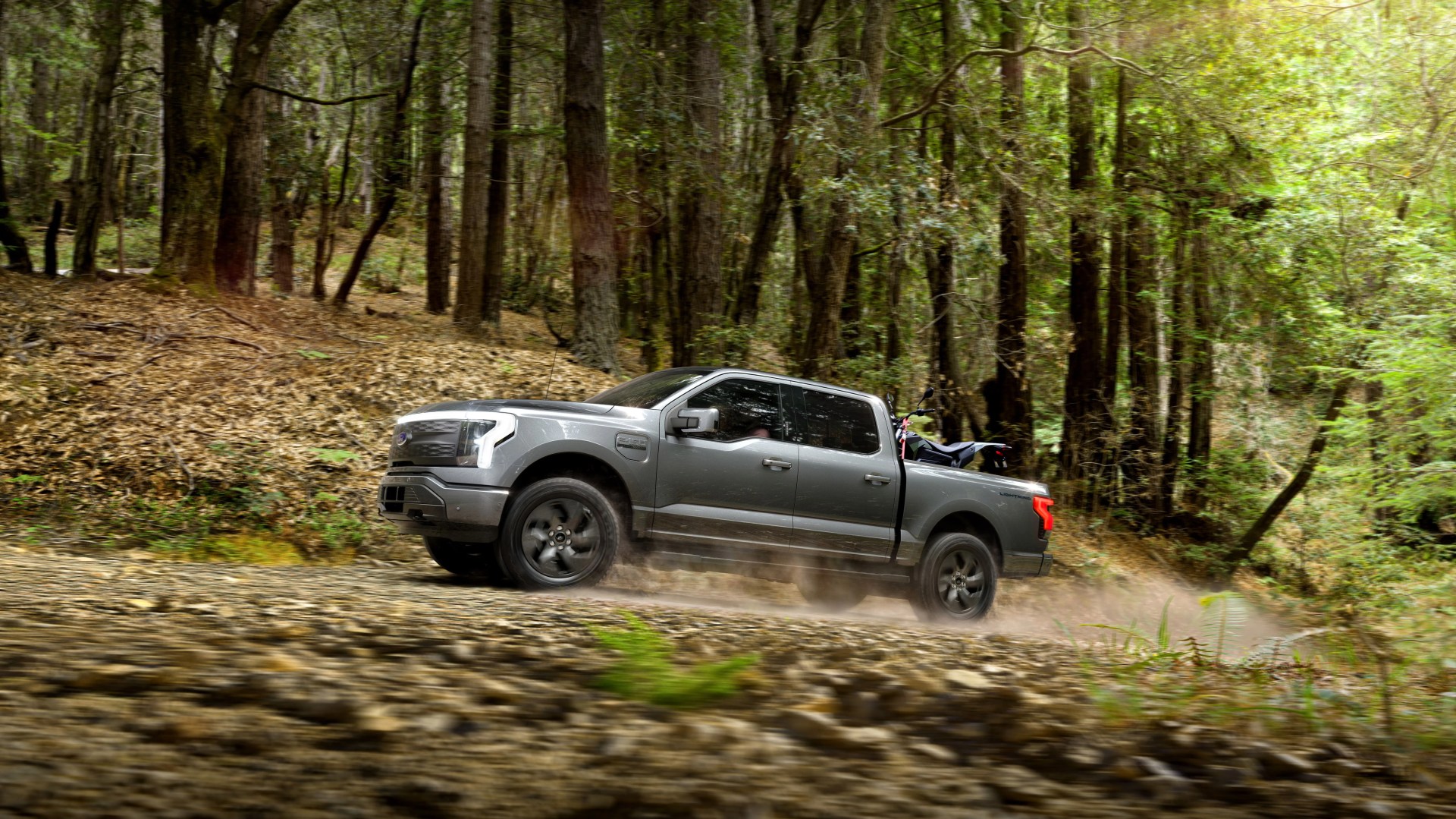 ford f 150 lightning driving in forest with a dirt bike in the bed