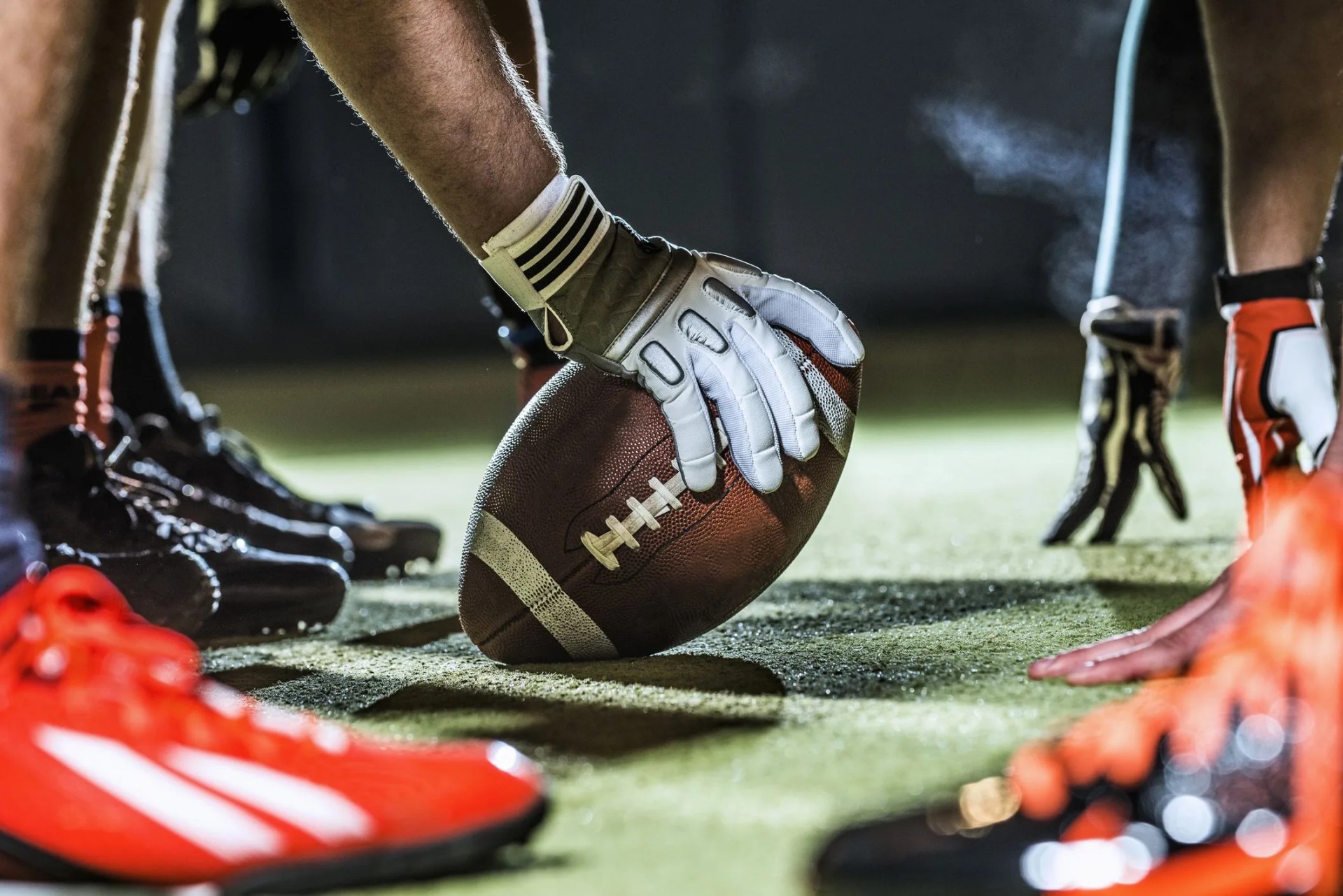 football on the ground, held by player wearing gloves on playfield