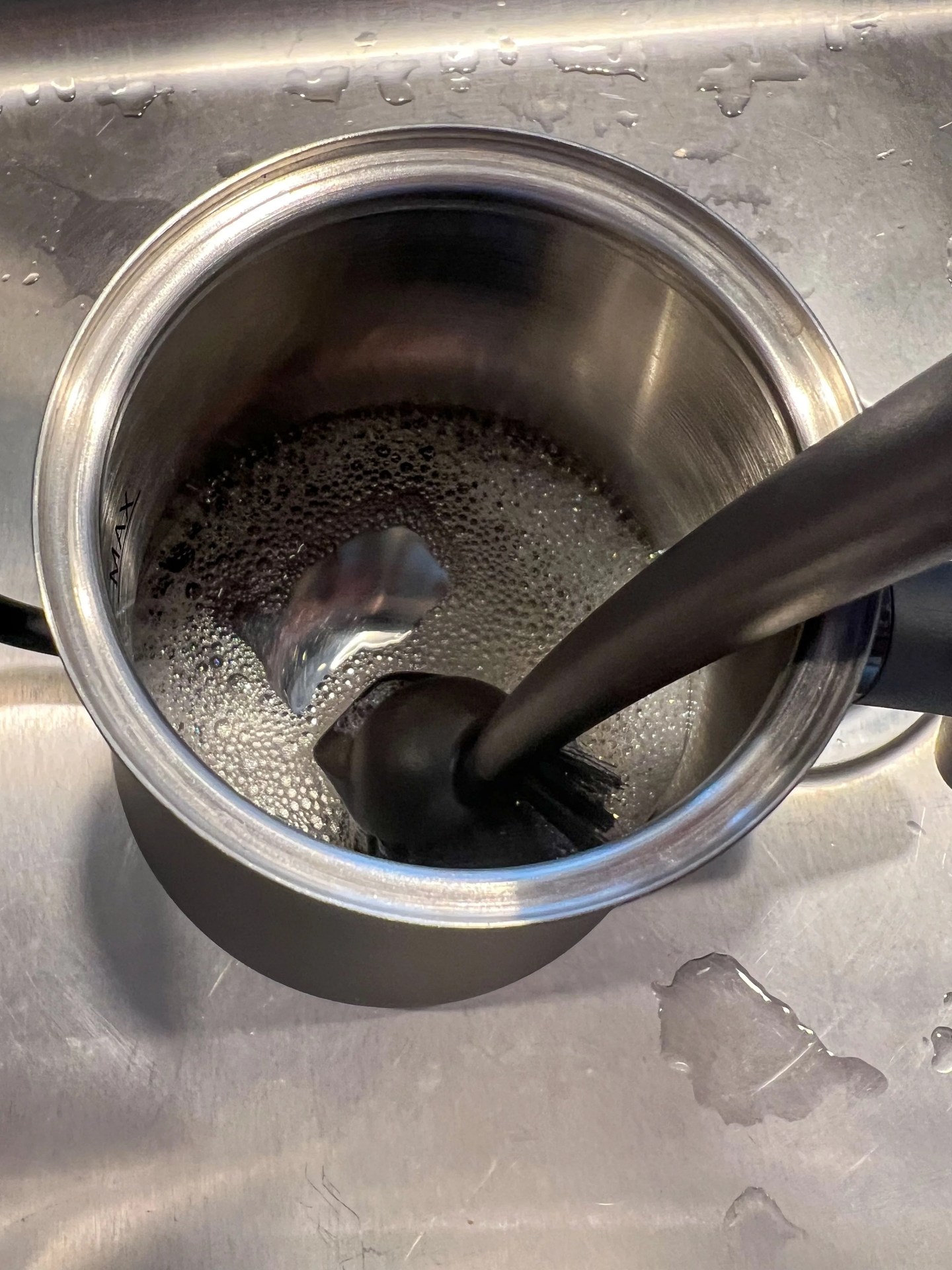 the soapy interior of an electric kettle being scrubbed in a sink