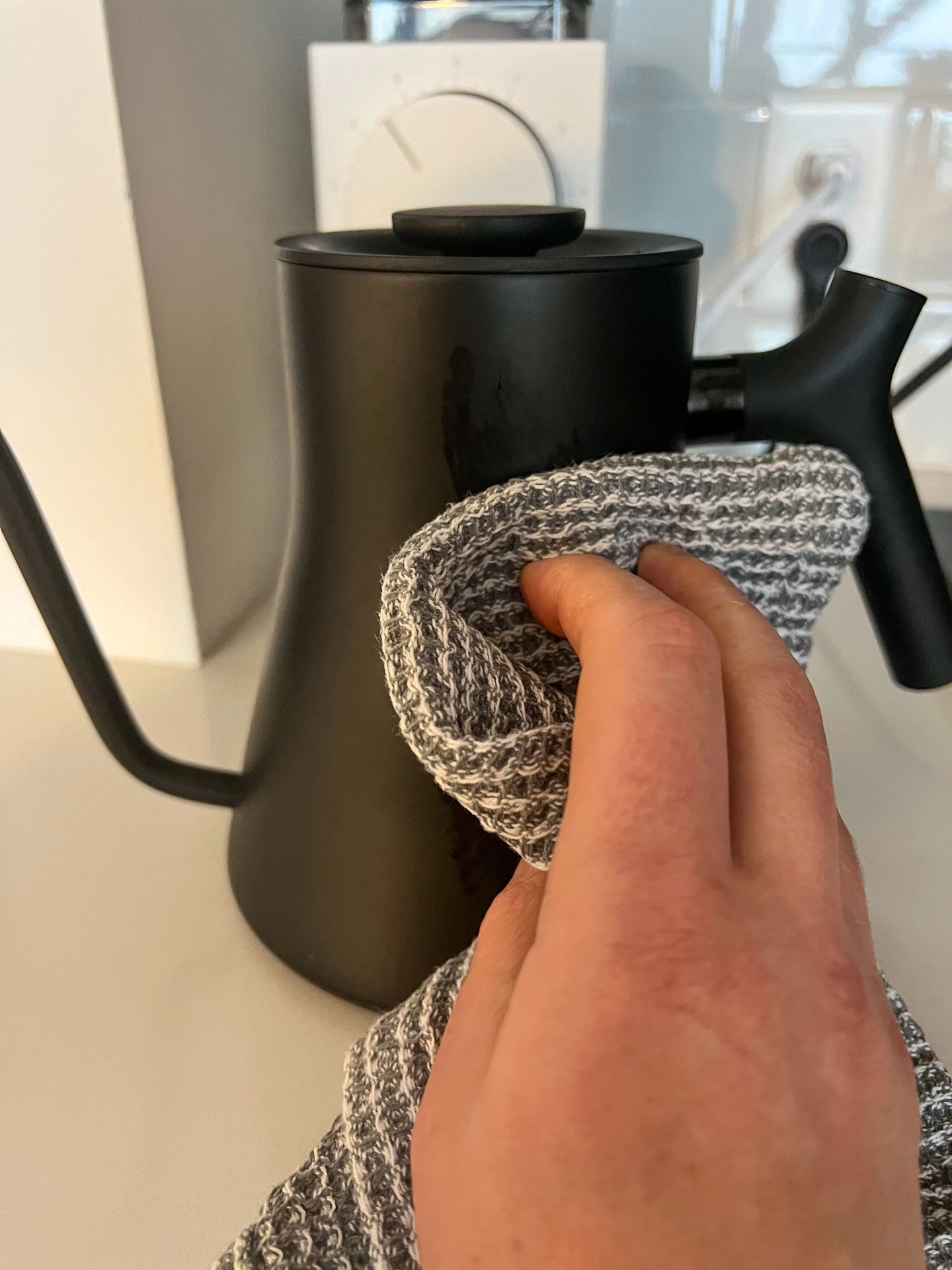 a person wiping down the exterior of an electric kettle