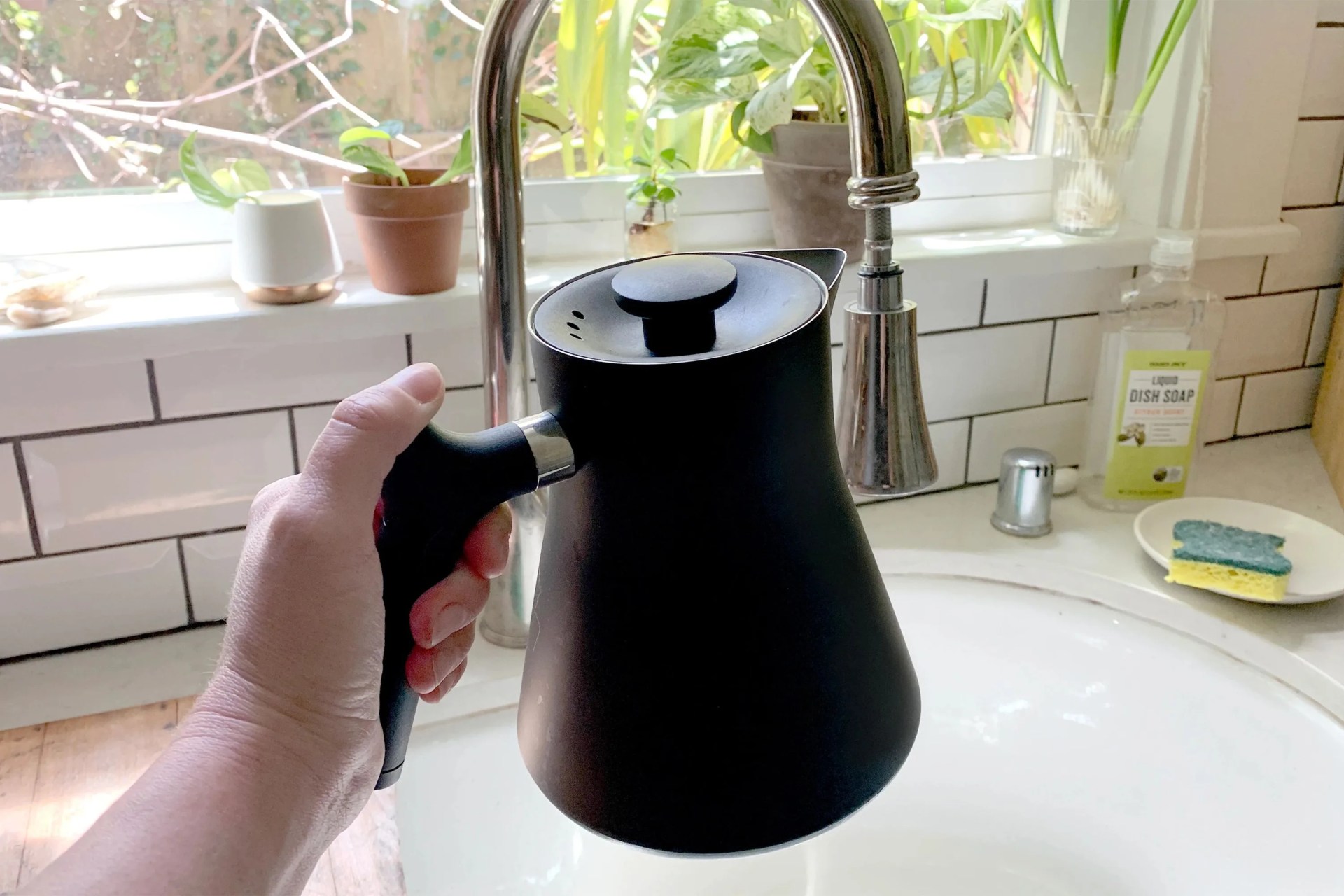 a person holding an electric kettle over a sink