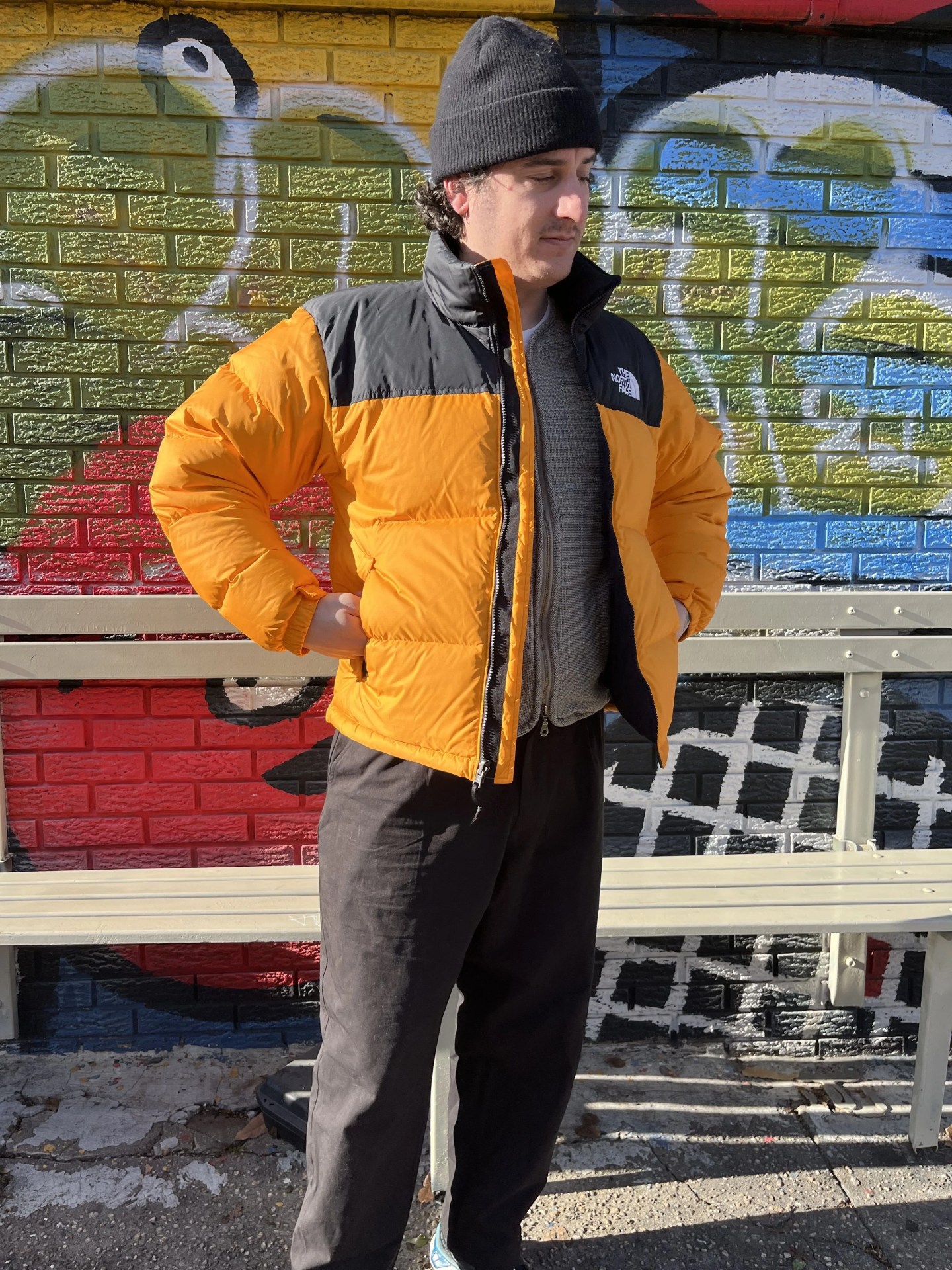 a man wearing a yellow puffer jacket standing in front of a graffiti wall