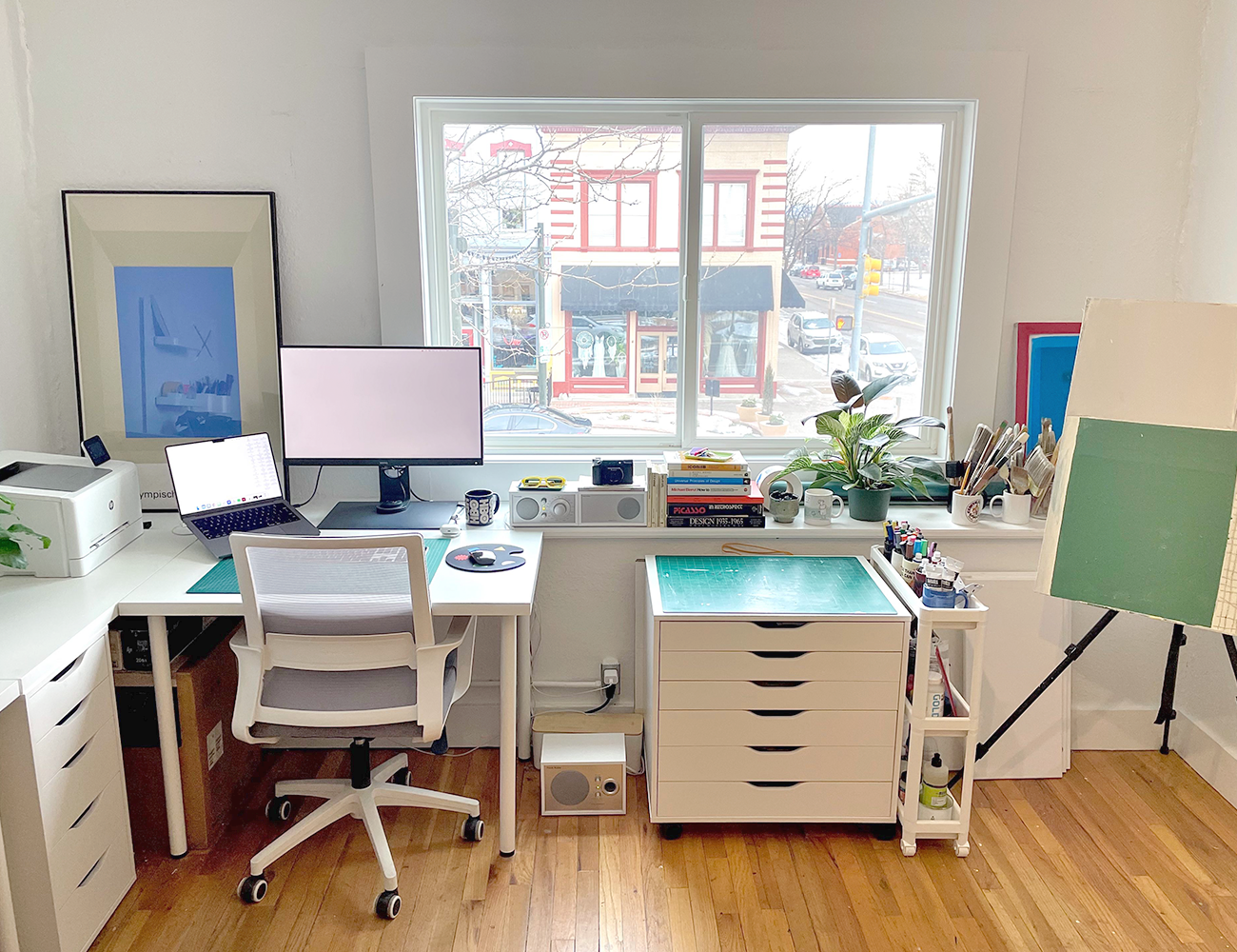 a photo of an at home desk set up with hardword floors, white walls, a white desk and a white flat file cabinet
