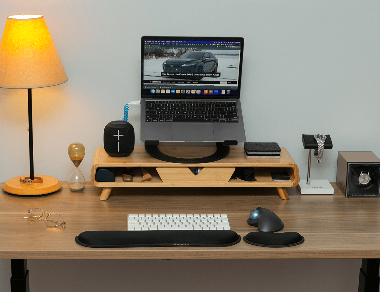 a light wood desk with laptop and lamp on it in front of a white wall