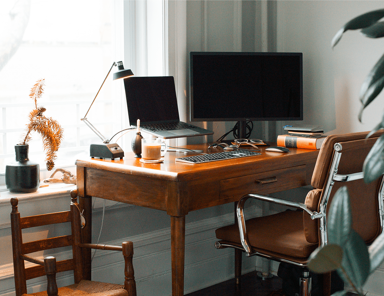a wood desk with two computer monitors and a black and silver chair in front of a white wall