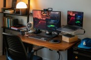 a photo of an office with brown desk 2 computer monitors and black chair and black bookshelf