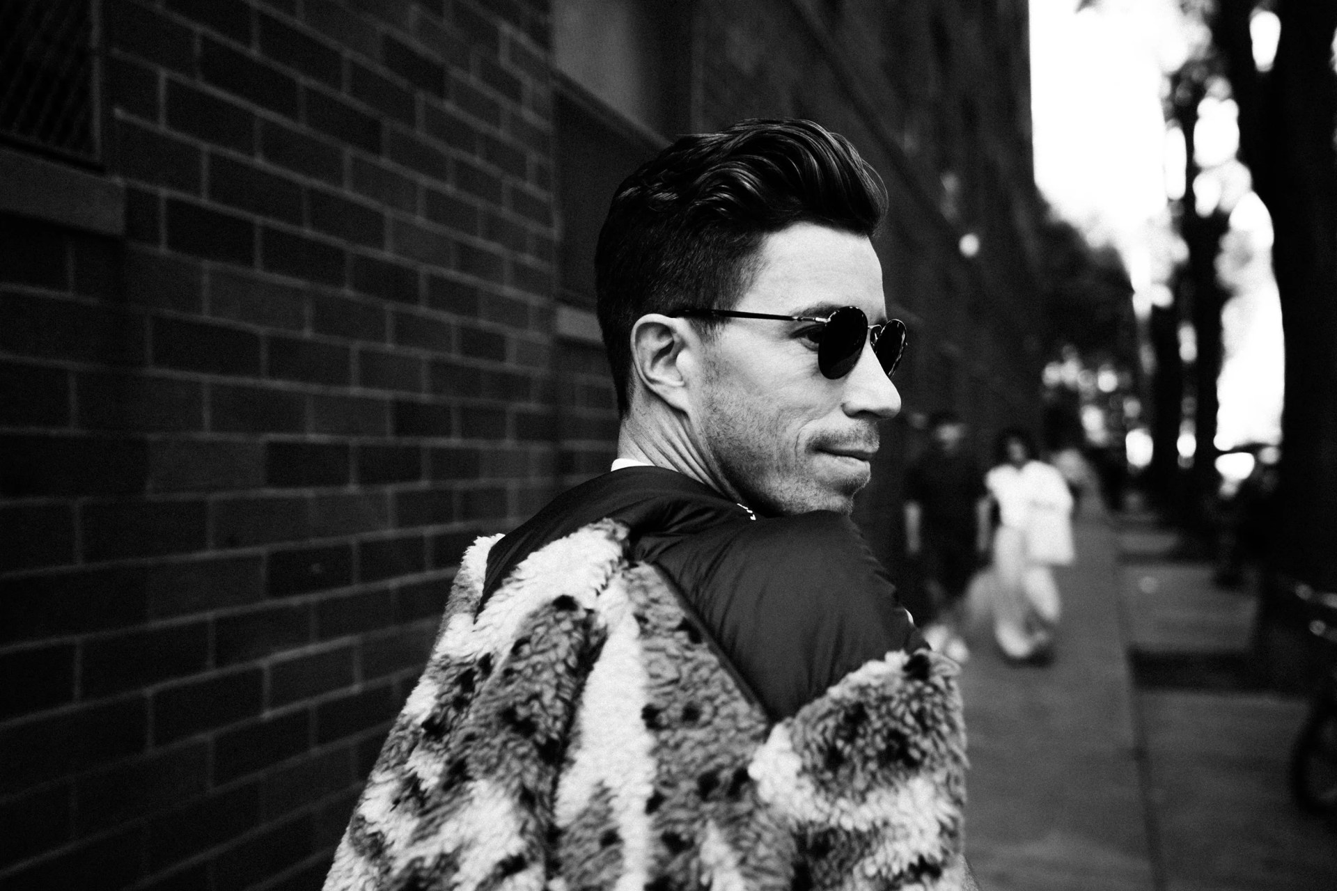 a black and white photo of snowboard shaun white walking down the sidewalk in sunglasses