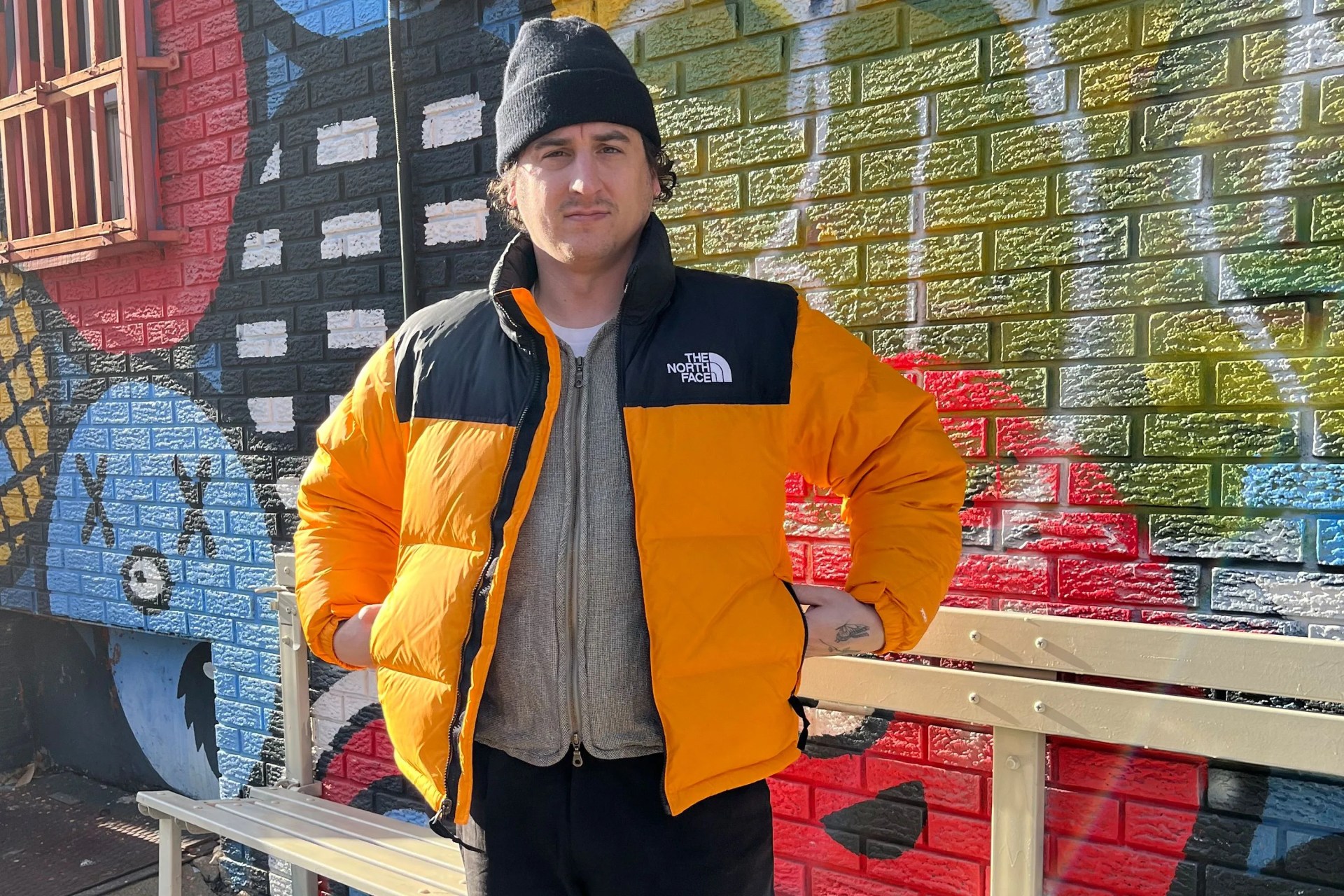 a man wearing a puffy zip up jacket and beanie standing in front of a graffiti wall