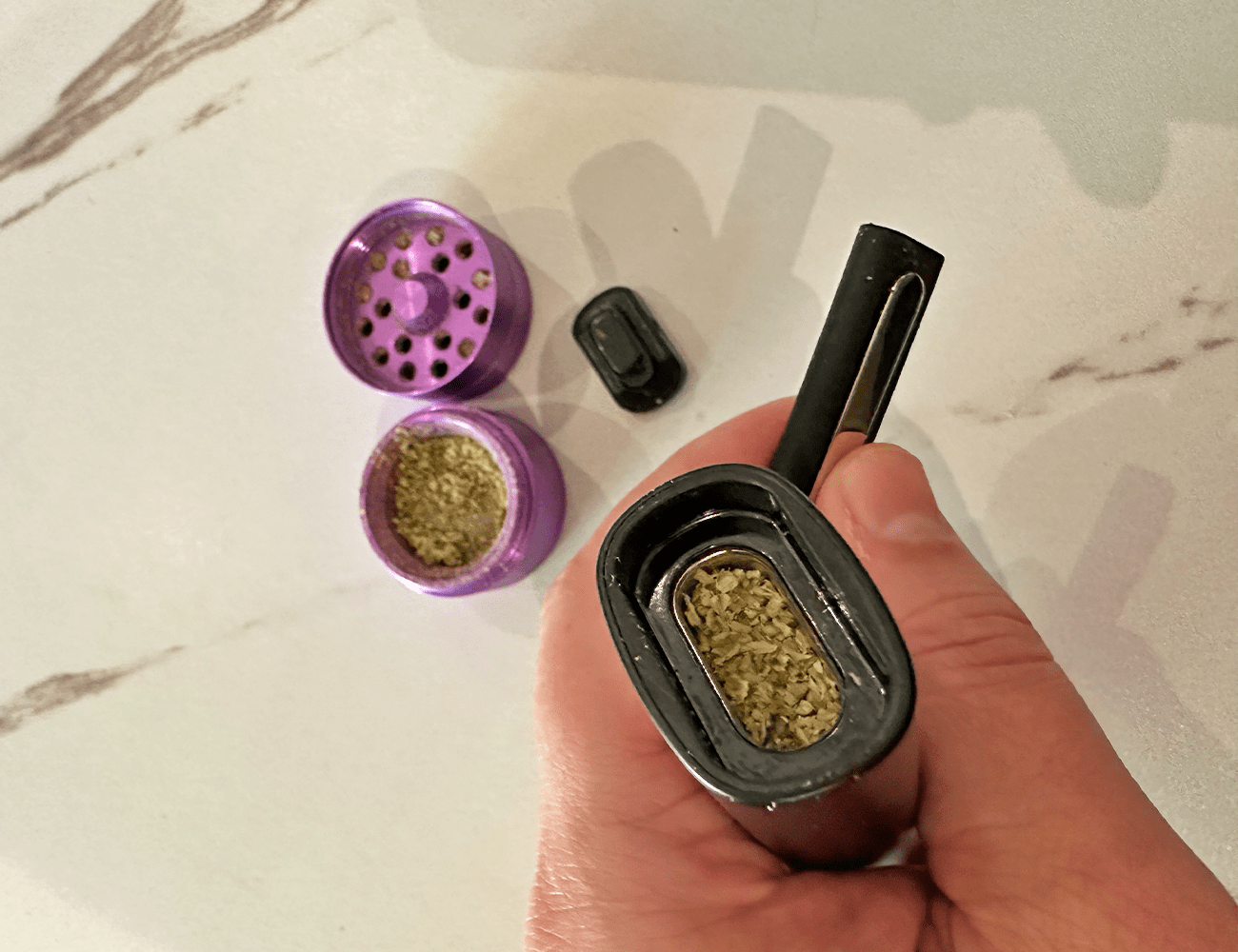 a hand holding a pax plus flipped upside down to fill the chamber with weed next to a purple grinder