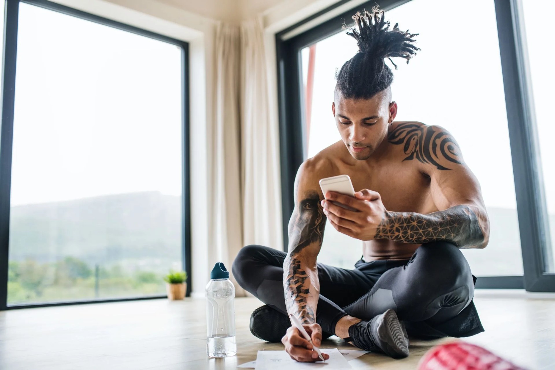 a portrait of fit mixed race man with smartphone doing exercise at home, checking progress