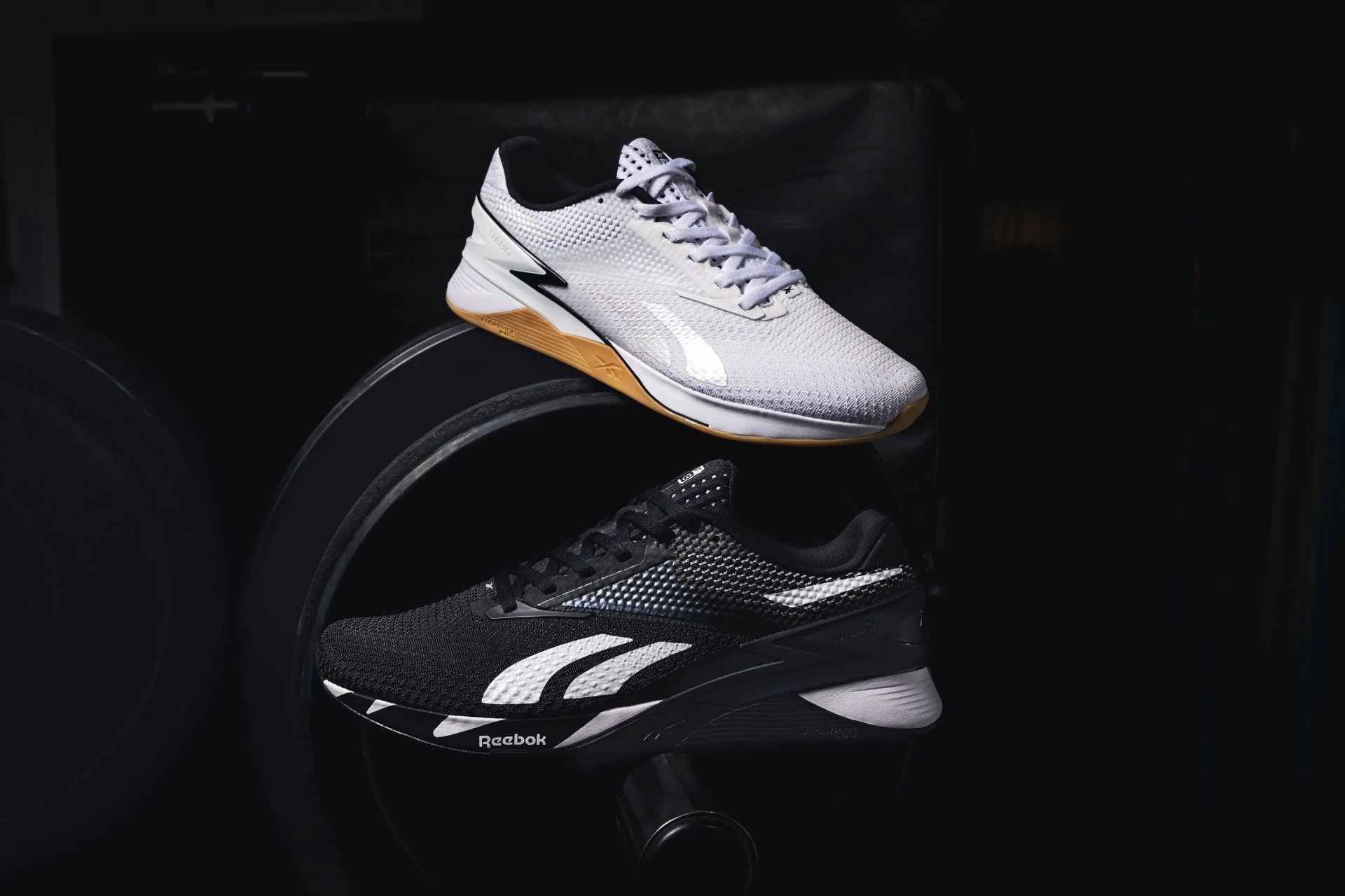 white and black nano x3 shoes sitting on top of weights in a gym