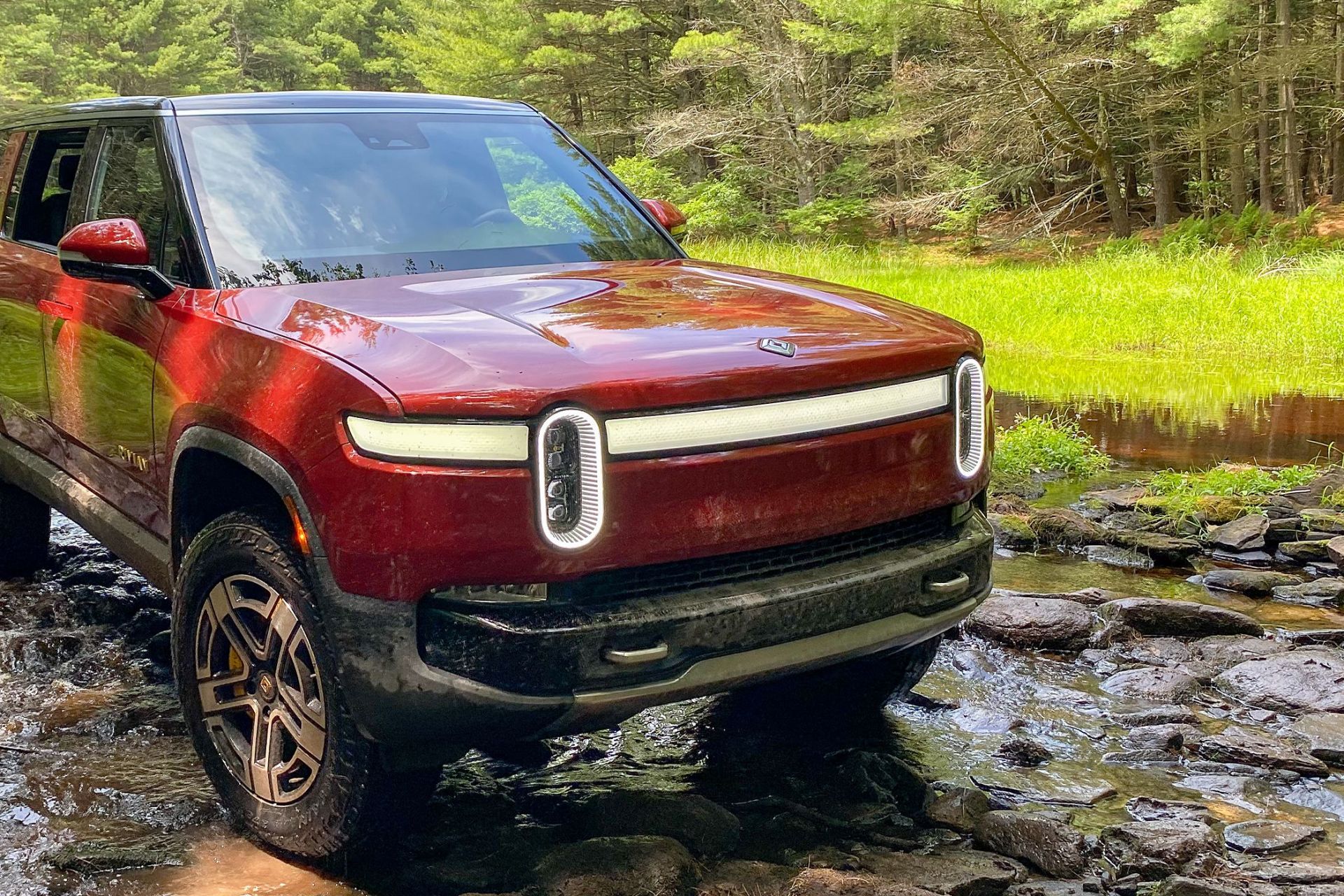 red rivian r1s parked in a rocky stream