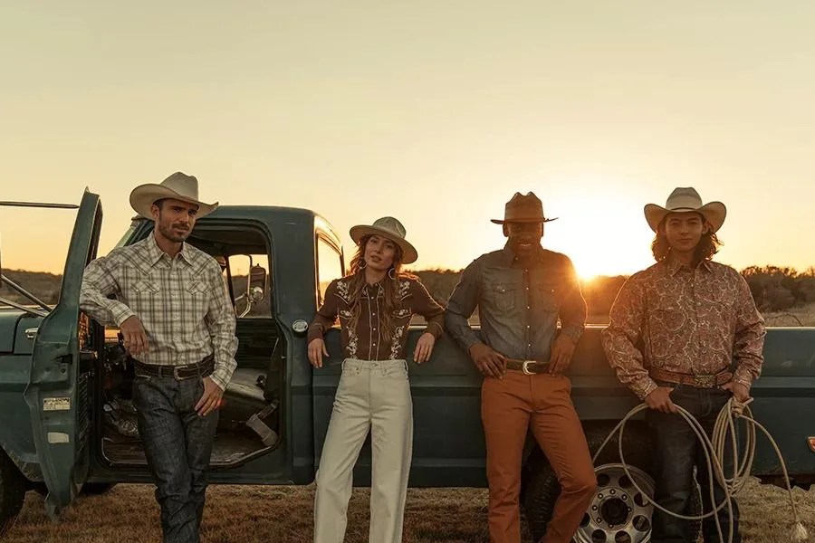 four people wearing cowboy hats leaning against an old truck on a ranch