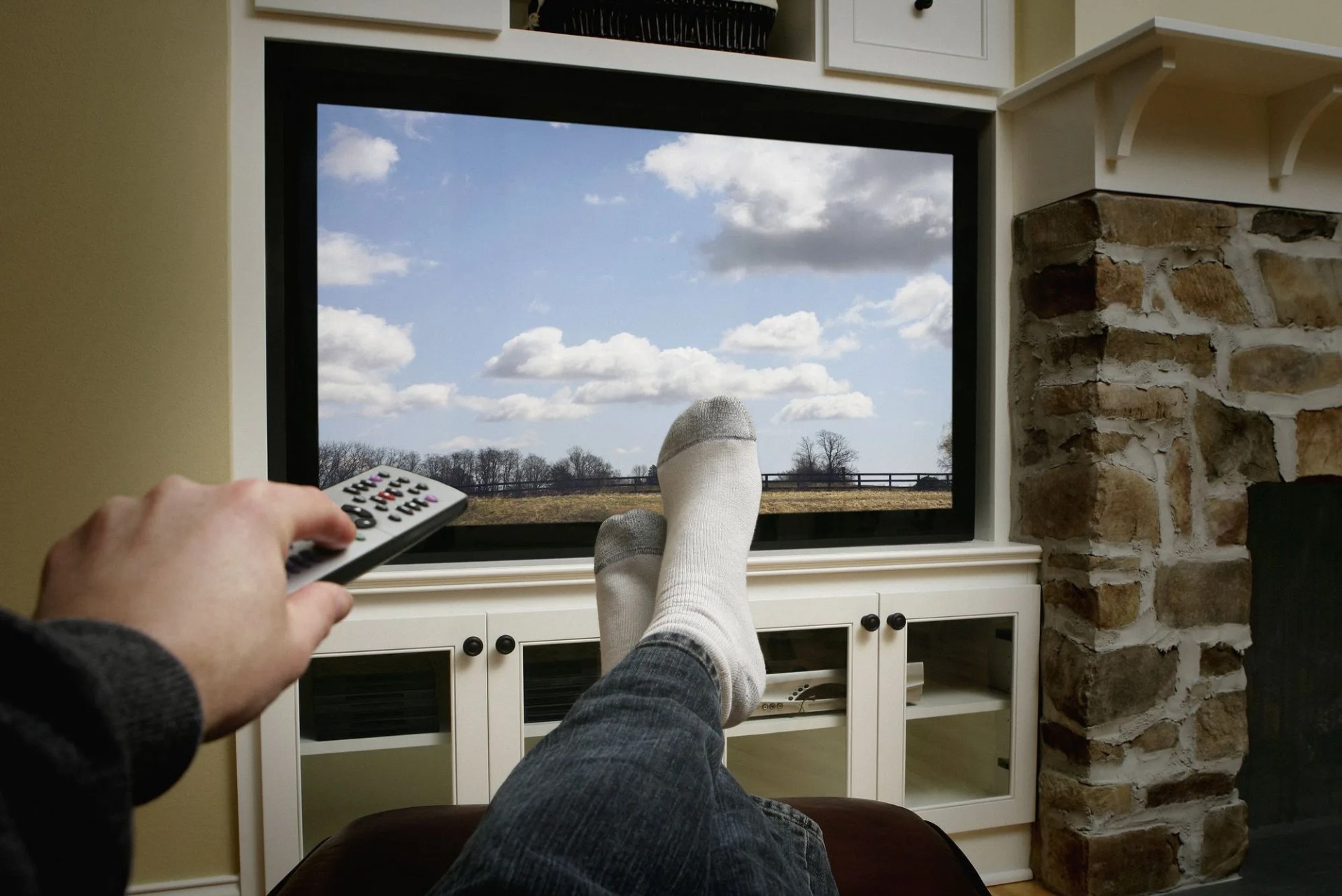 using remote with feet in front of flat screen