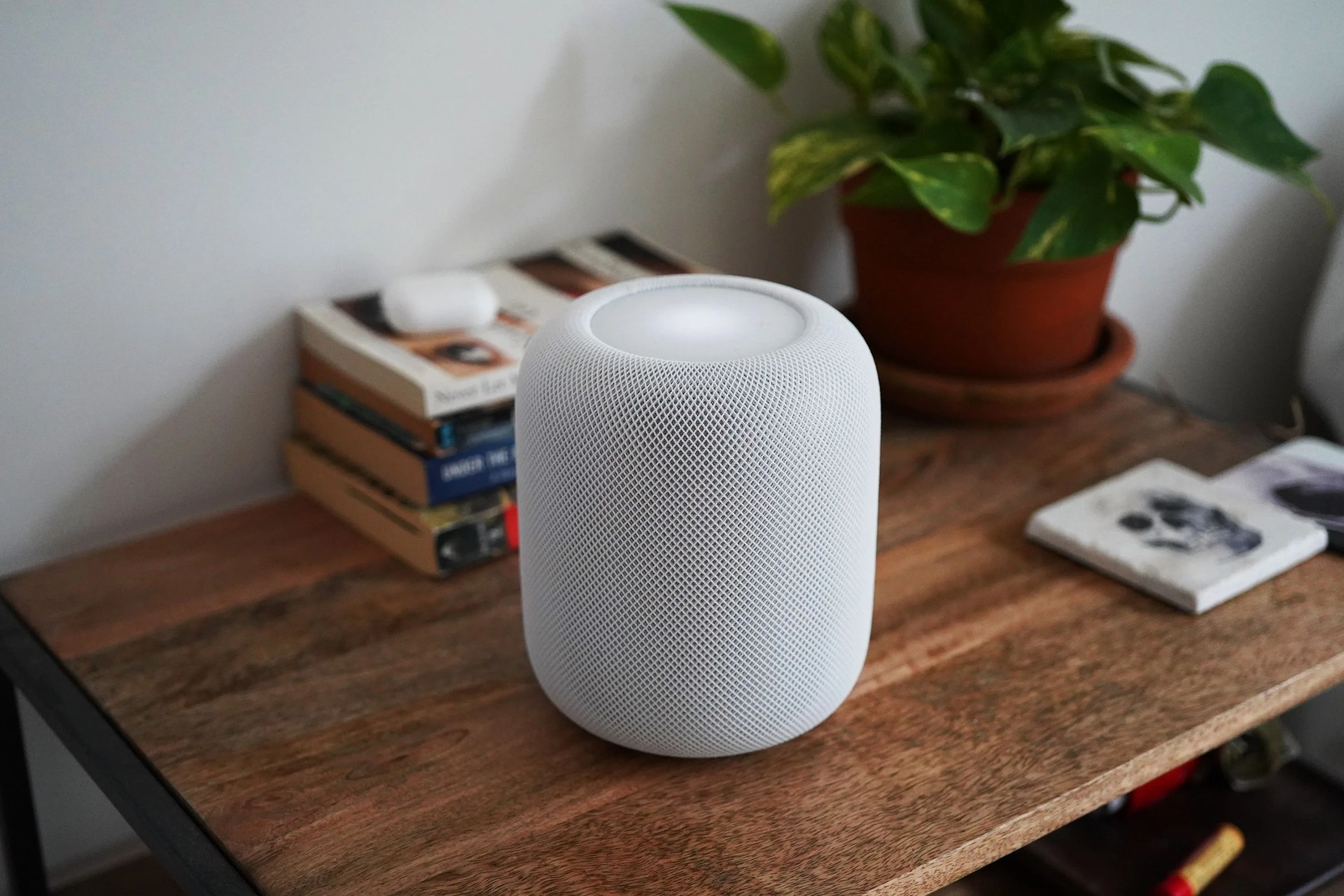 white homepod device sitting on a brown wood coffee table with books and green plant in the background