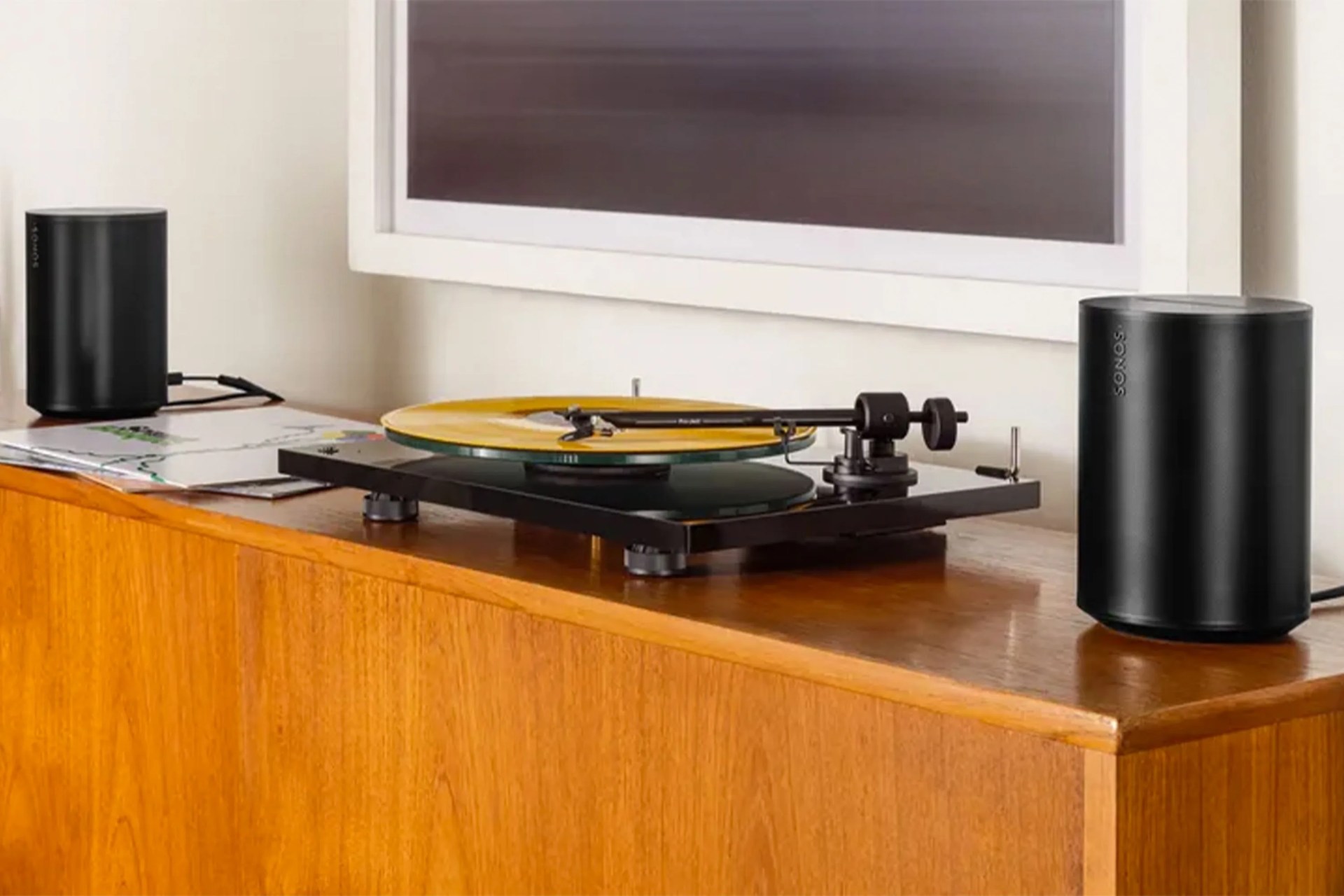 sonos speakers on a table with a record player and a tv hanging on the wall above