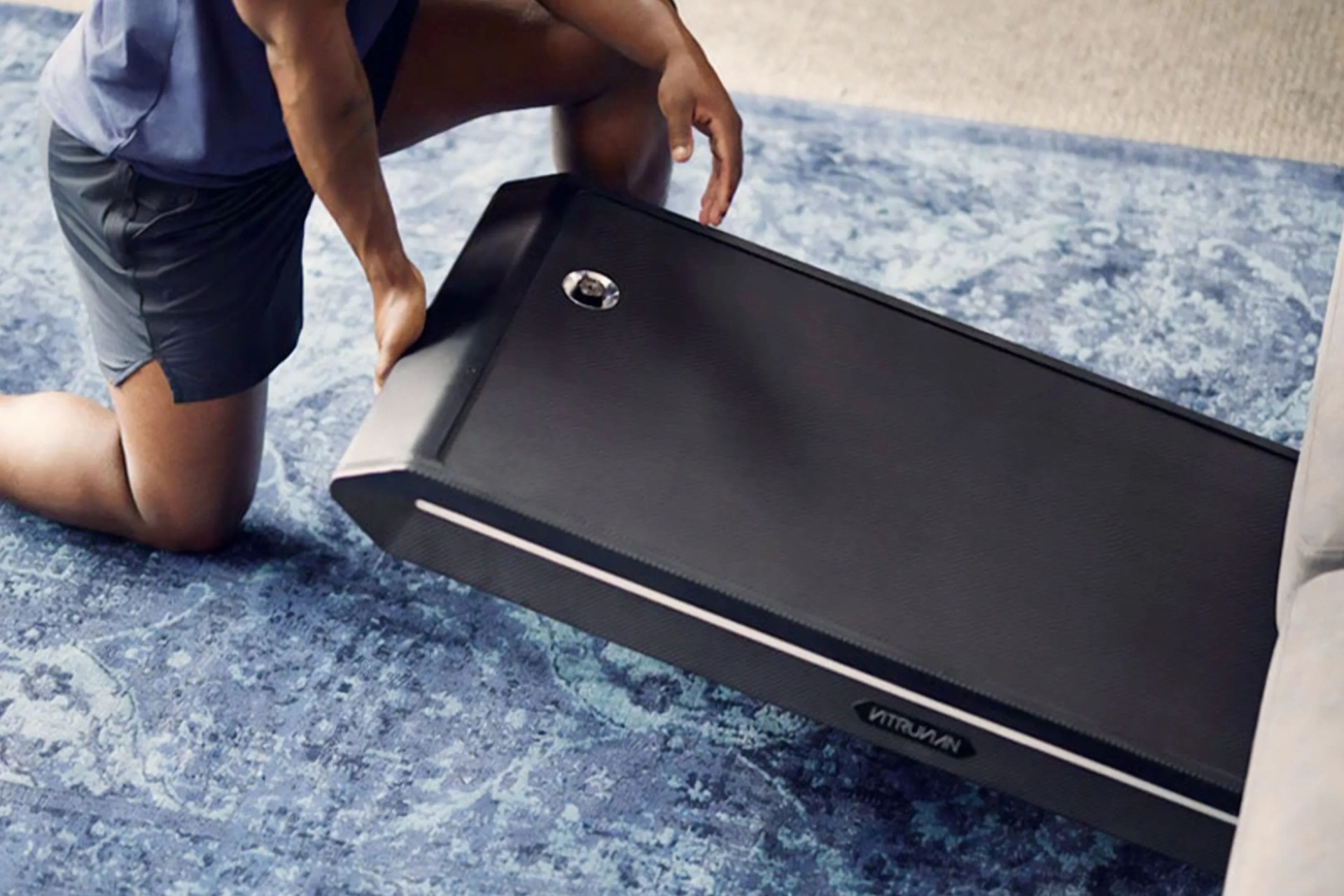 a man sliding a vitruvian trainer plus under a couch