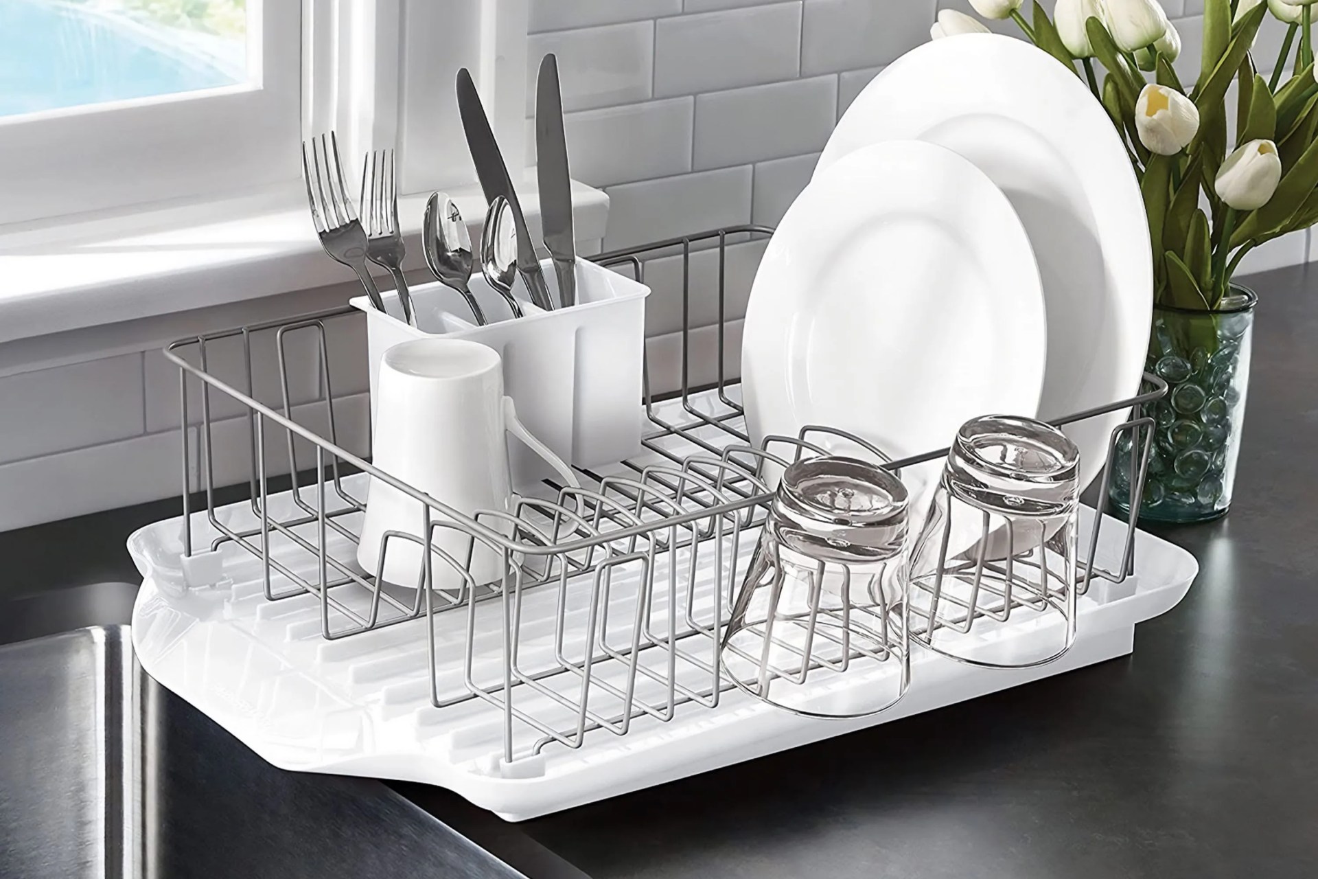dishware in a drying rack next to a sink with a vase of white tulips