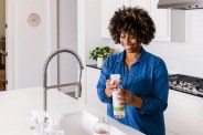 a woman filling up a cleaning bottle by a sink in a kitchen