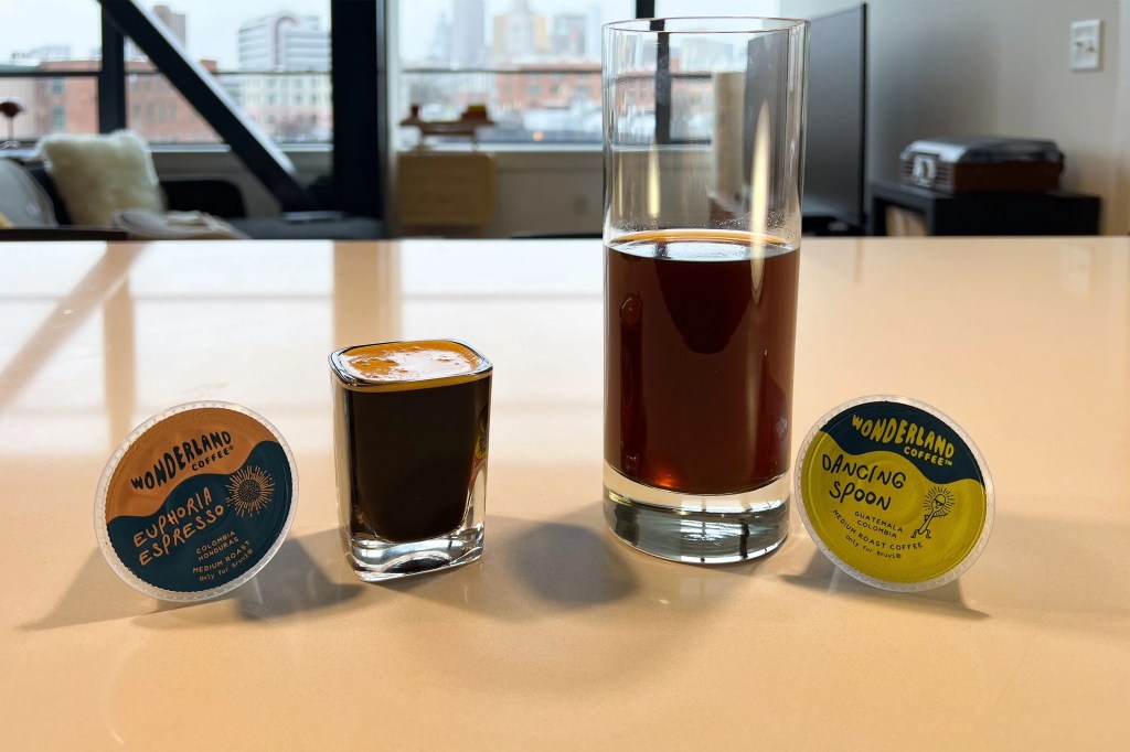 a shot of espresso next to a cup of coffee with 2 coffee pods on a countertop
