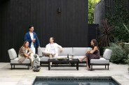 people sitting on a couch on a pool patio with drinks, snacks, and a dog