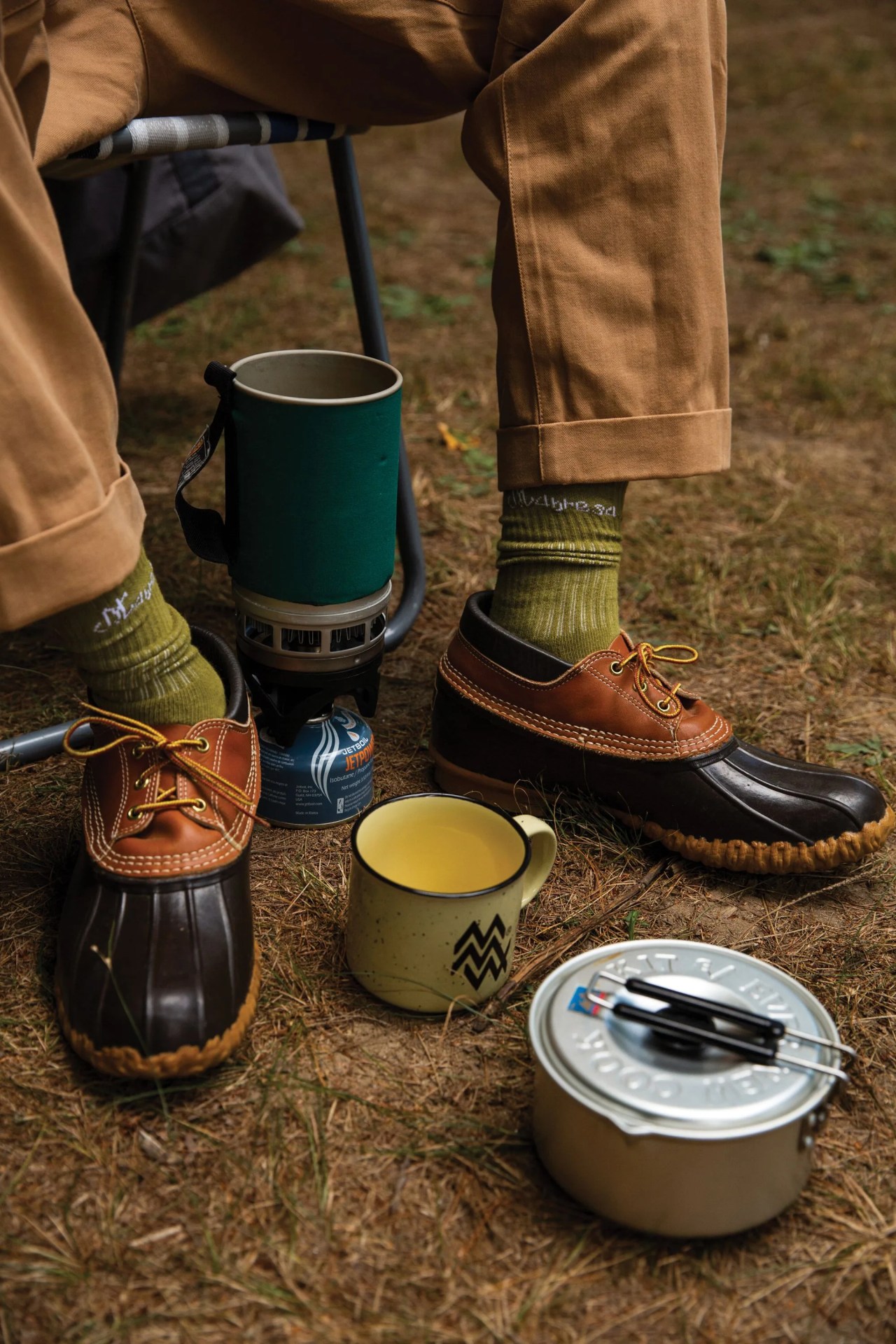 a person with camping supplies wearing rain boots, socks, and rolled up pants