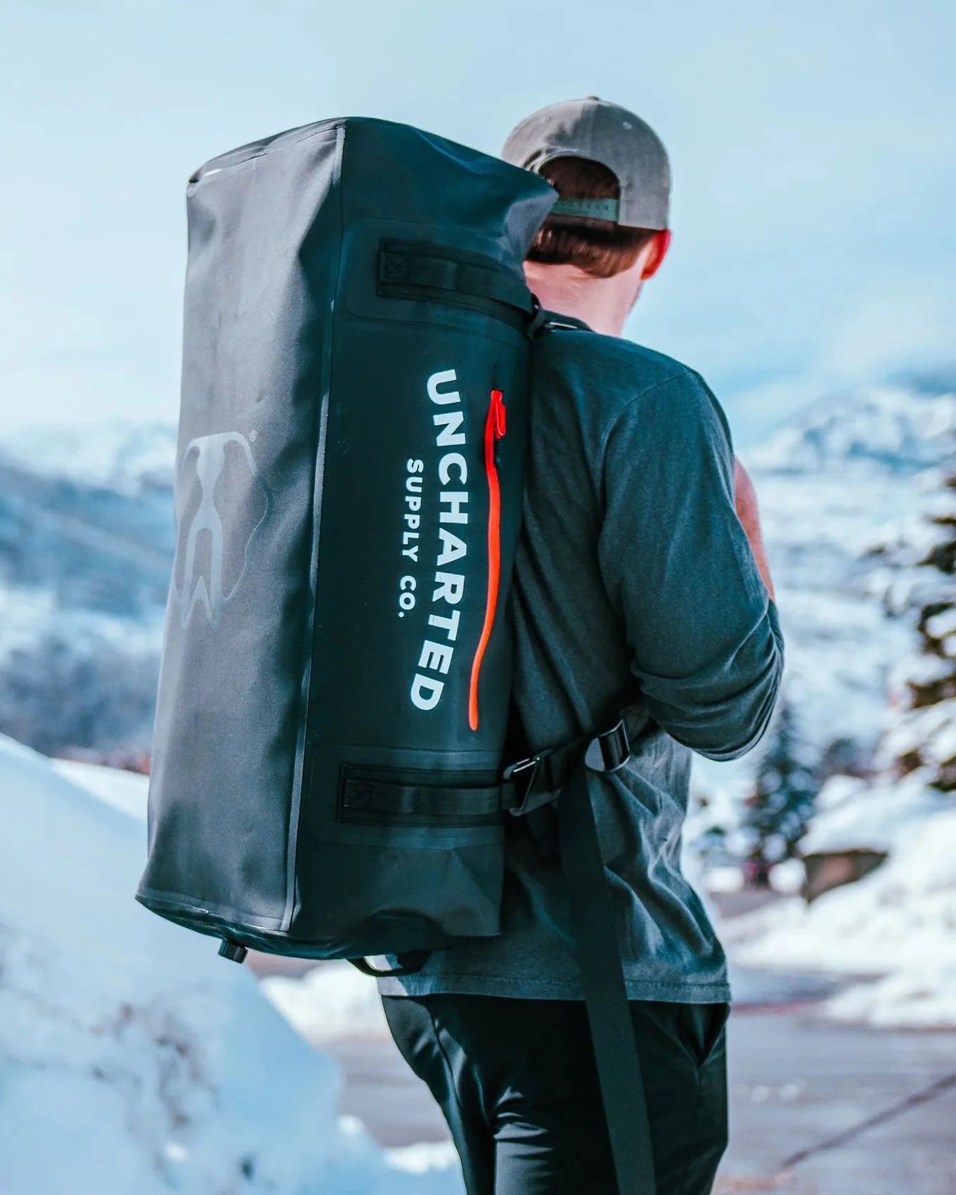 man carrying uncharted supply company the vault 65l duffel bag on his back walking in snow