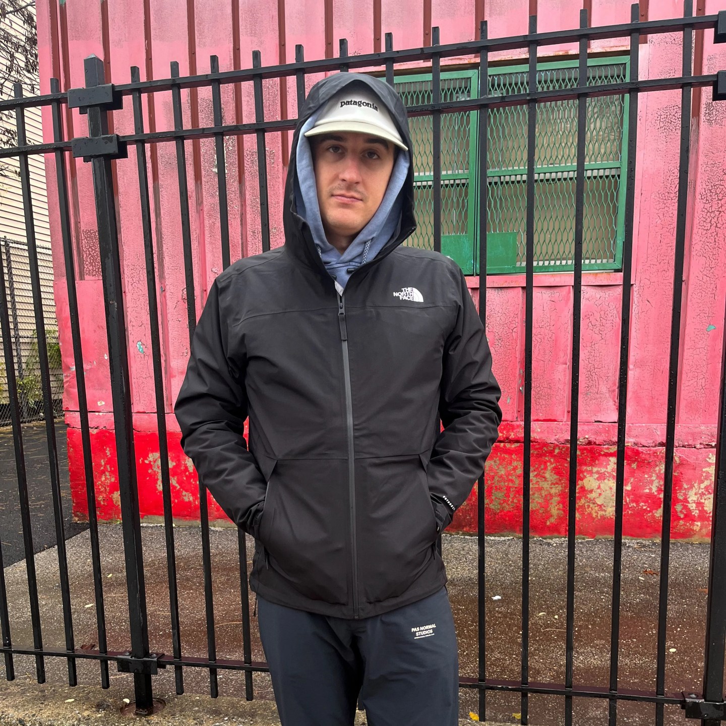 man standing by a fence wearing a north face rain coat