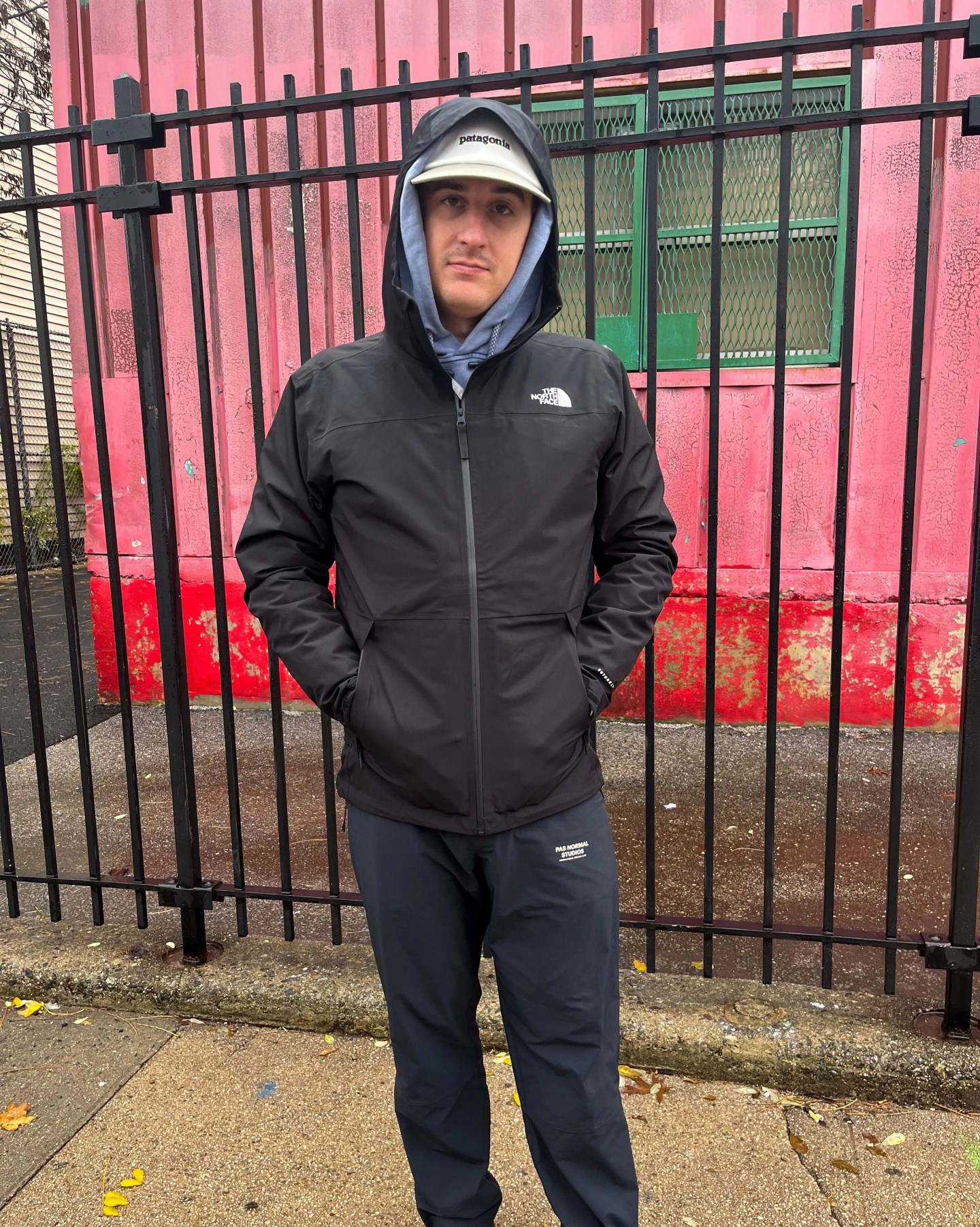 man standing by a fence wearing a north face rain coat