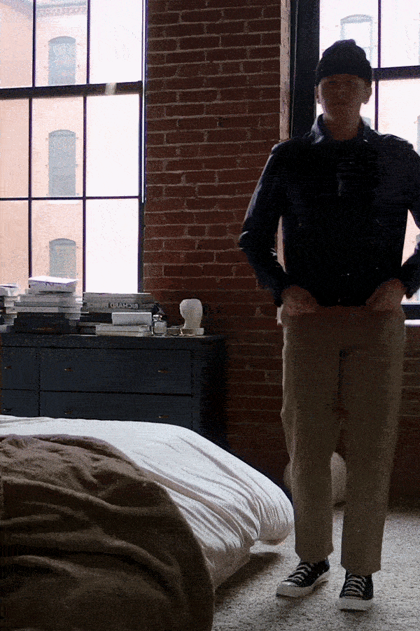 man wearing a leather jacket, khaki pants and black sneakers showing off how the clothes fit