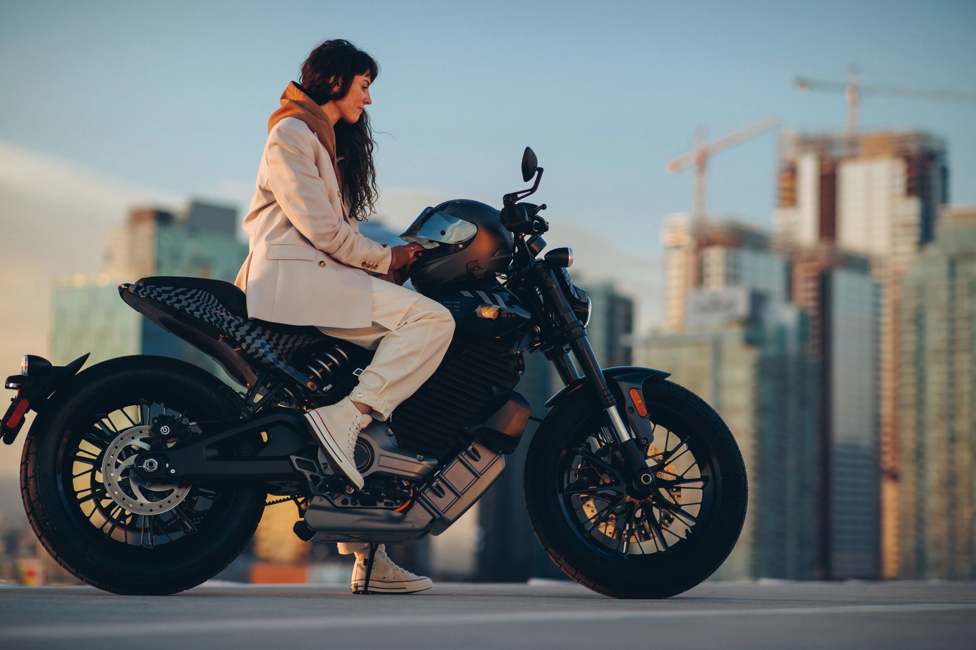 woman sitting on parked livewire s2 del mar electric motorcycle with city skyline in the background
