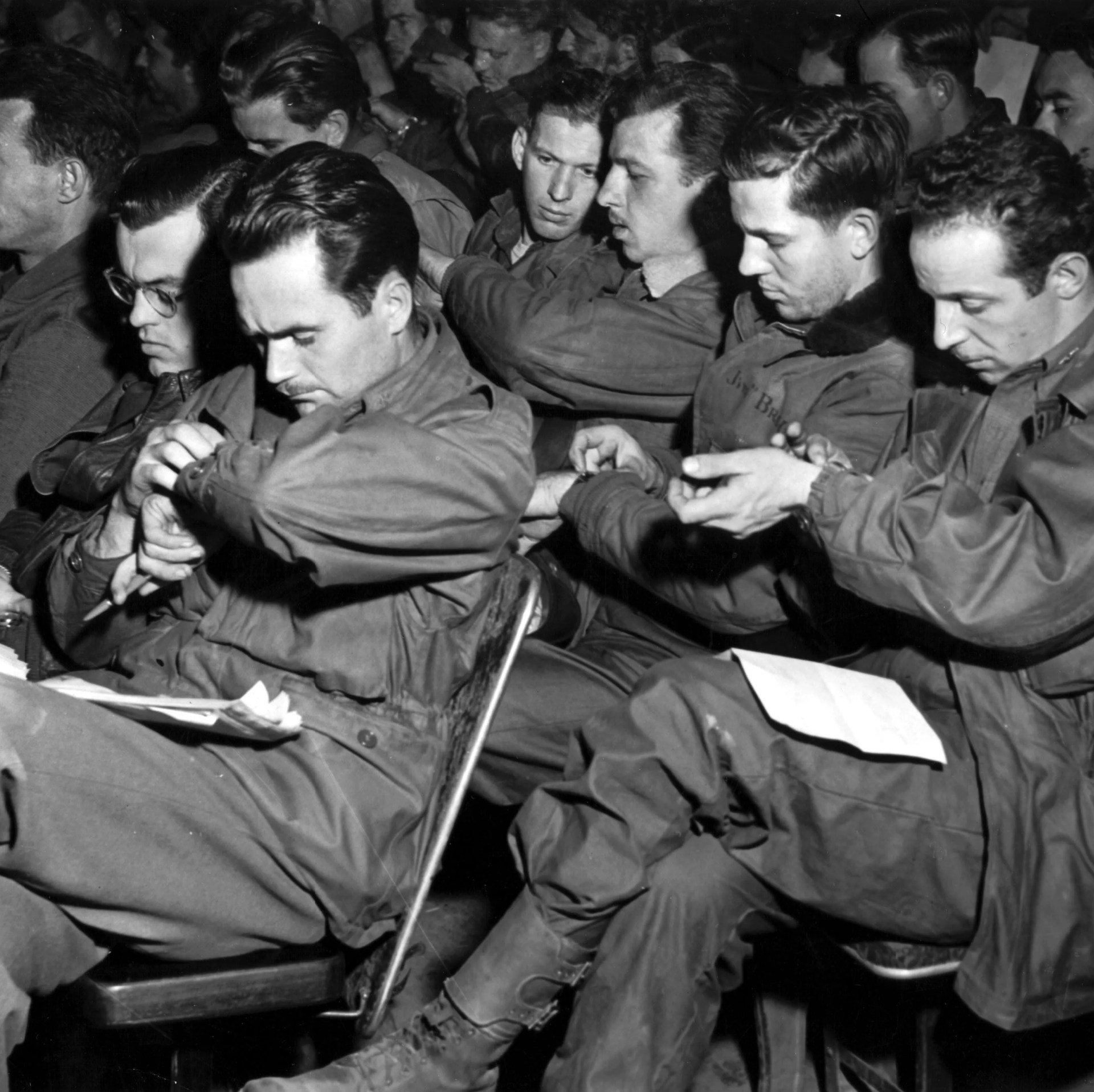 men of a us troop carrier group, 1st allied airborne army, synchronize their watches during a briefing preceeding the droping of paratroopers and gliders troops east of the rhine river