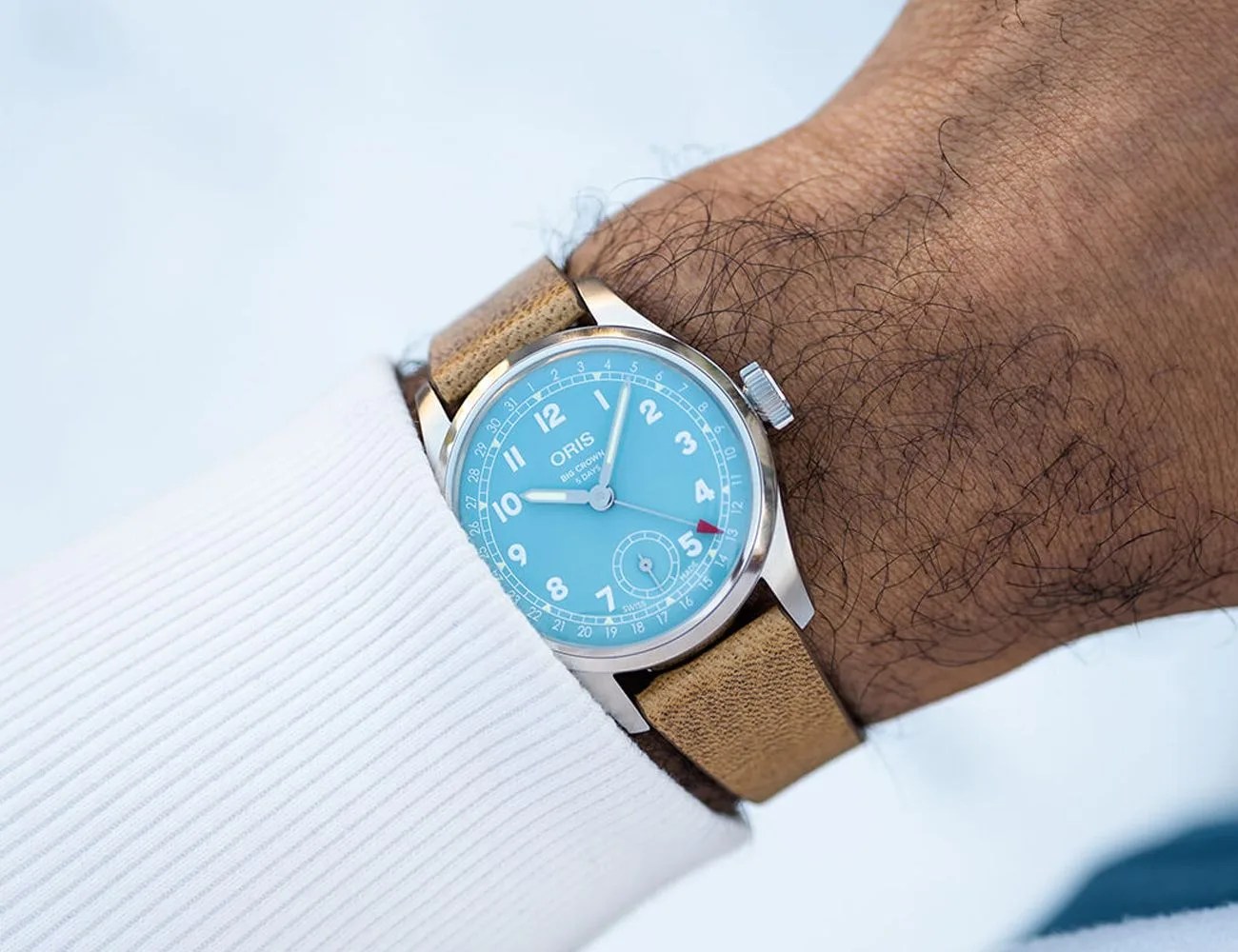 a watch with a brown strap and light blue dial on a mans wrist