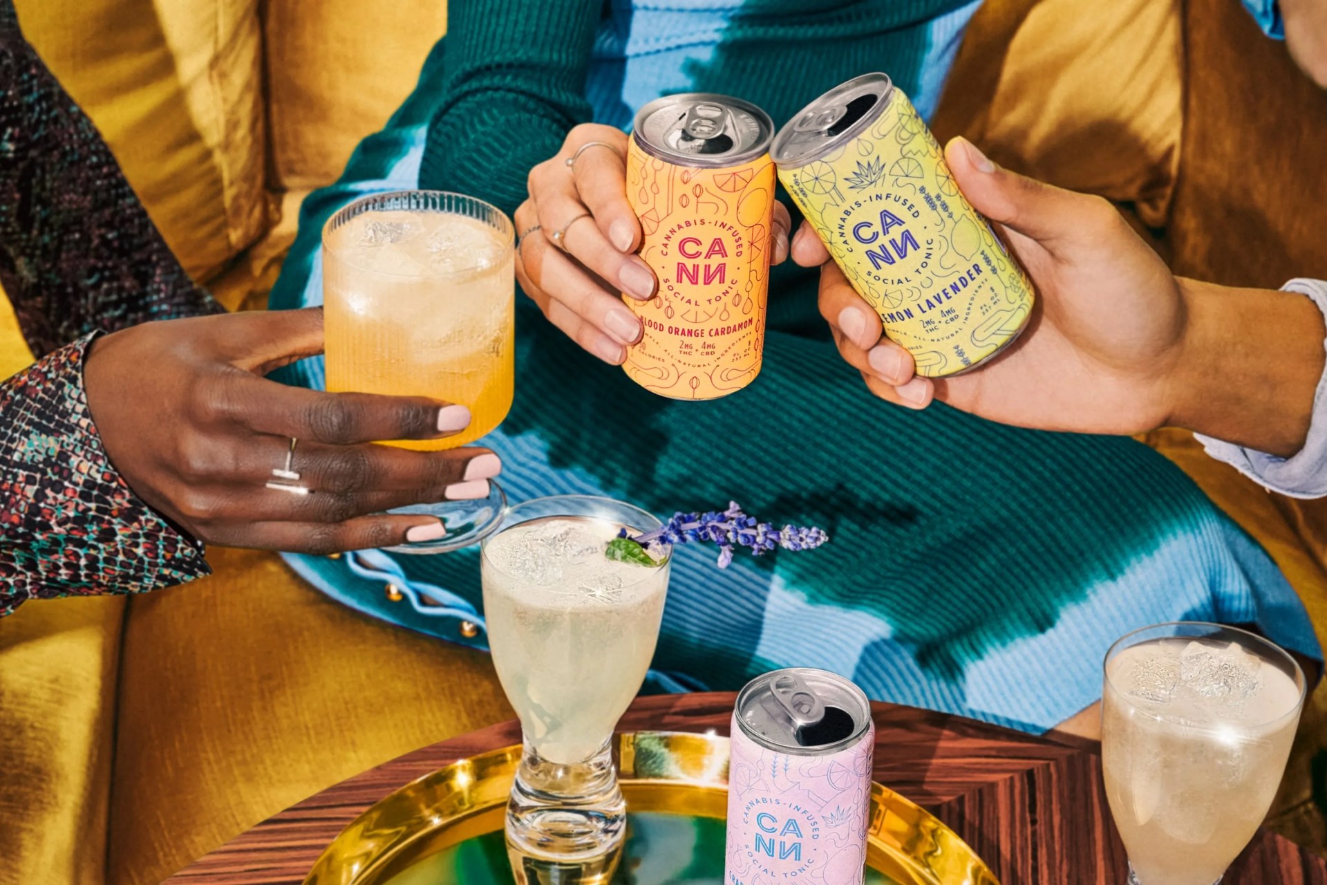 people cheersing cans and cocktails around a table