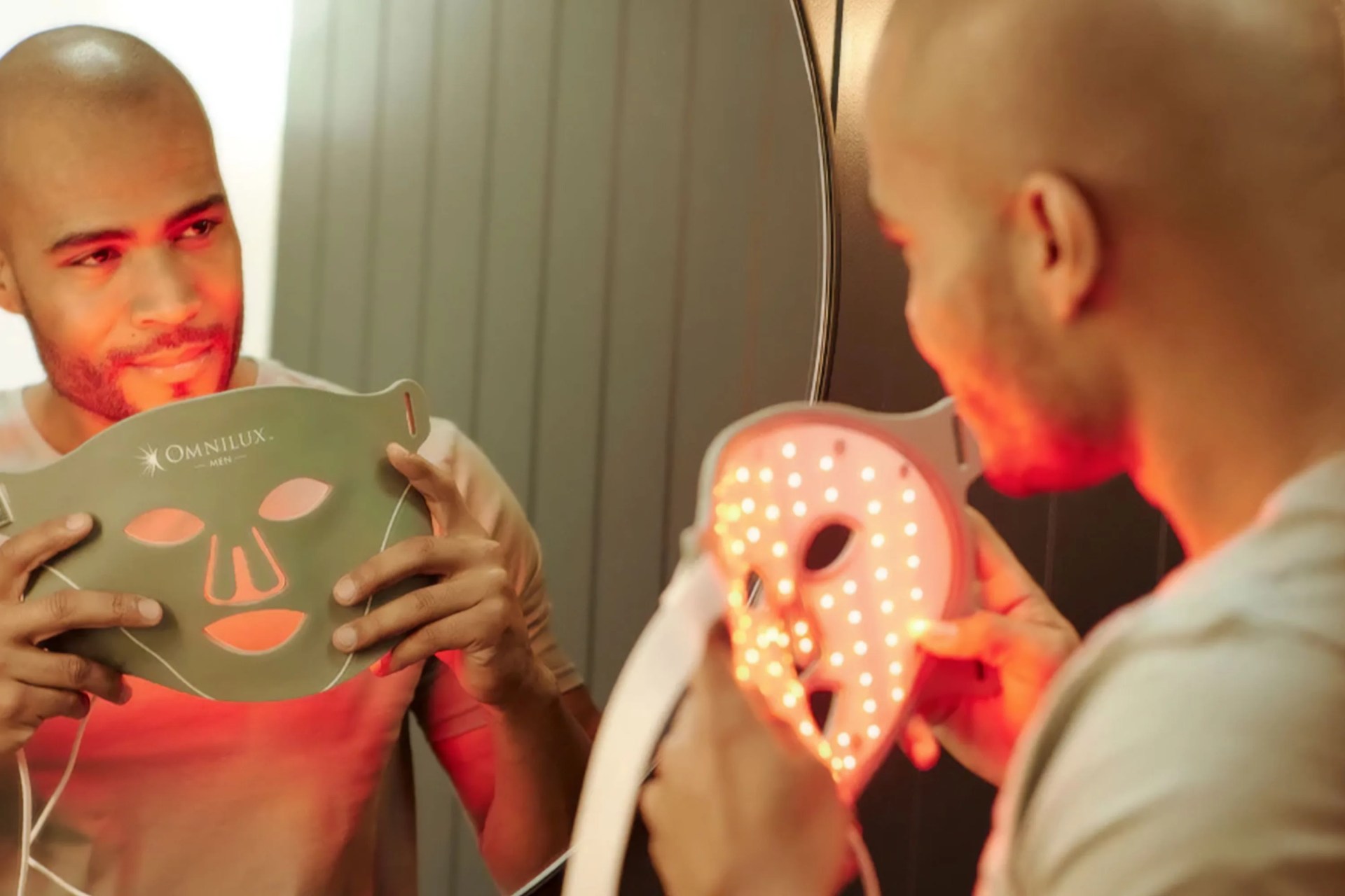 a man looking in a mirror holding a omnilux face mask