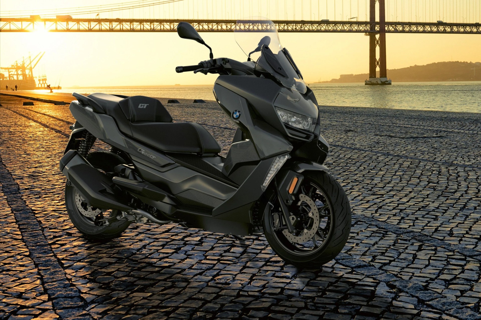 bmw c 400 gt motorcycle parked in front of a bridge in the distance with sunset in the background
