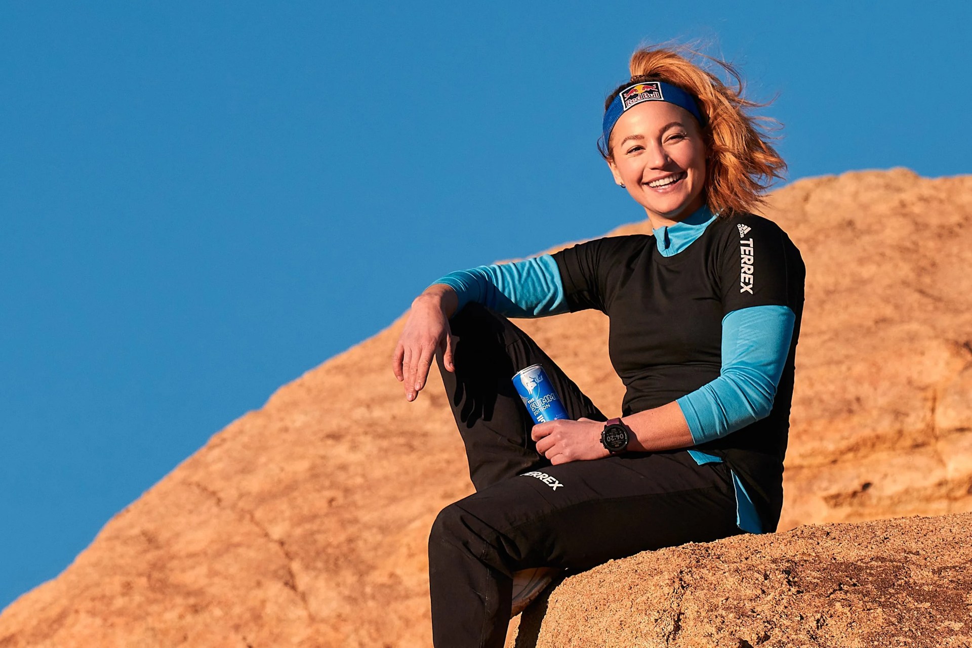 a woman climbing on rocks with a red bull can