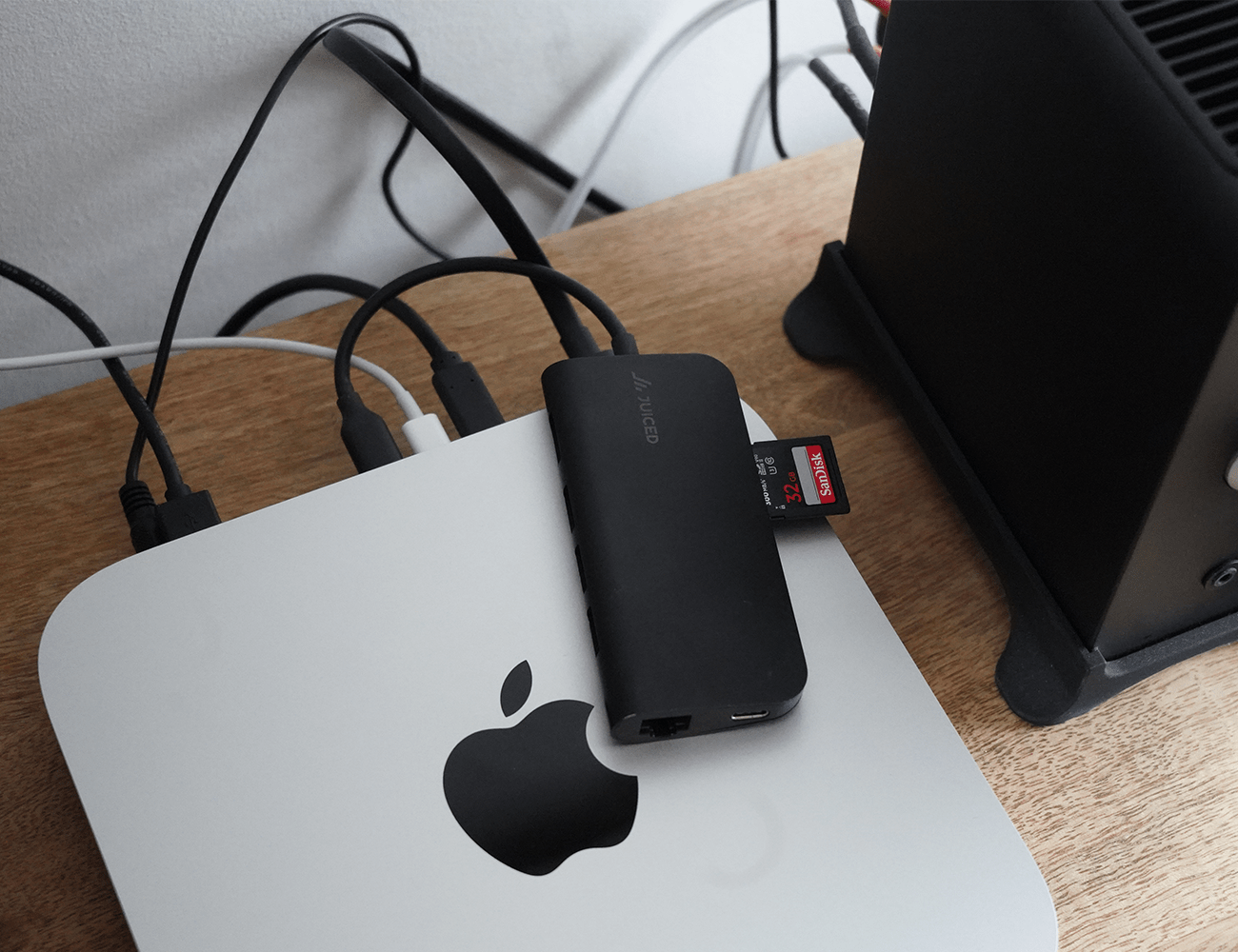 a brown desk with a silver mac mini and black cords on it