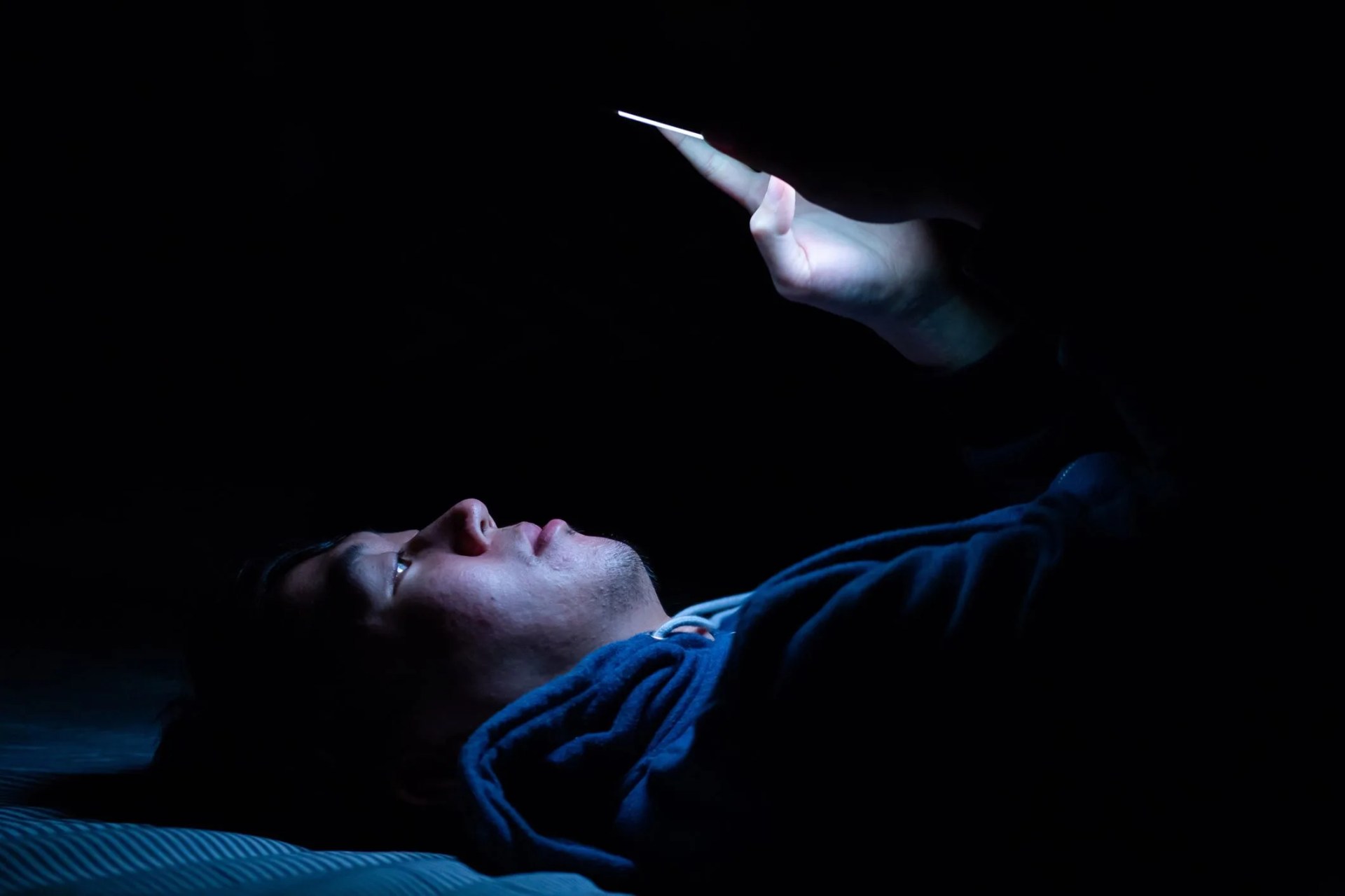 asian young man using phone in dark bedroom with blue light phone screen unhealthy eyes strain concept