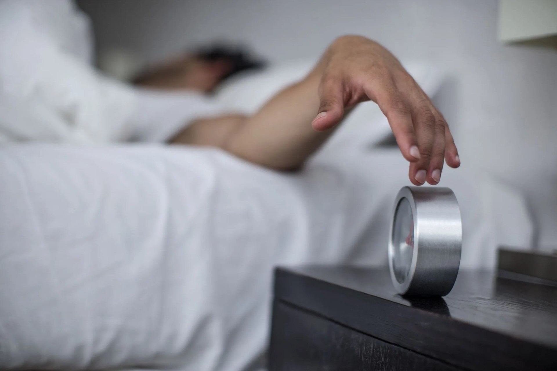 man reaching to turn off alarm clock