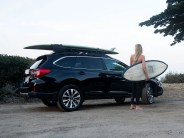 front runner roof rack on car holding surfboard with woman standing next to it