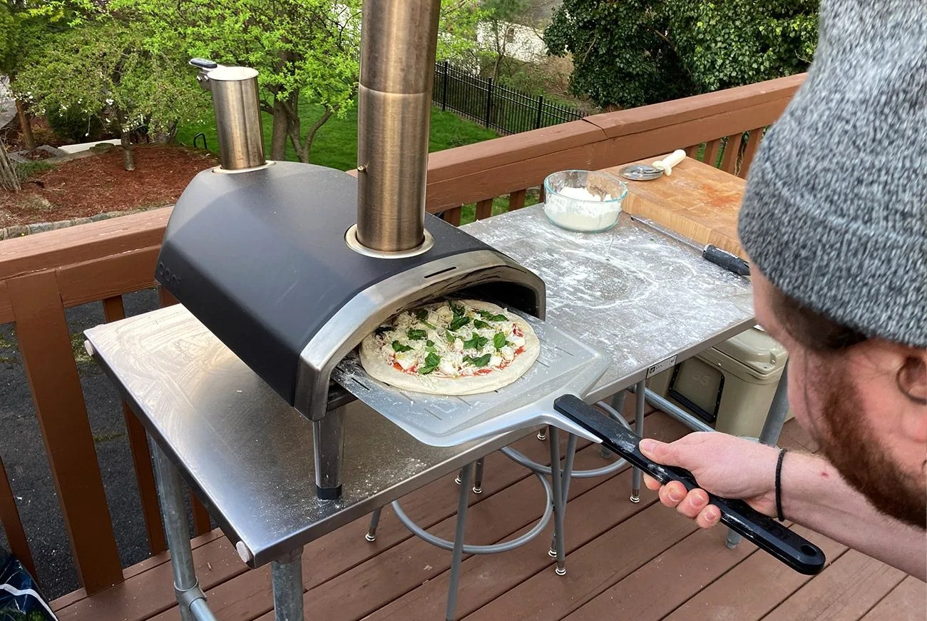 person putting a pizza into the ooni fyra pizza oven