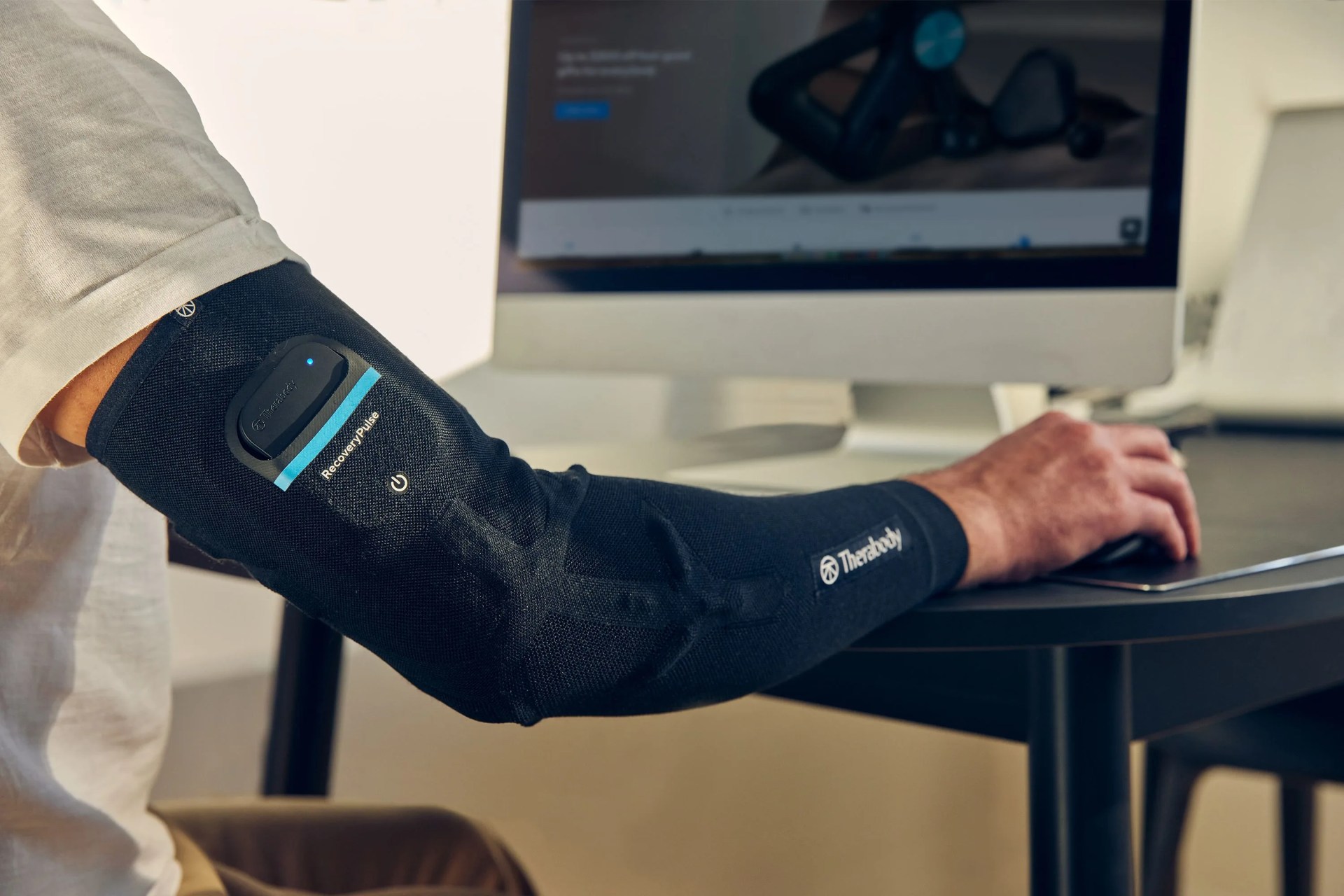 a person wearing a therabody sleeve while working on a computer